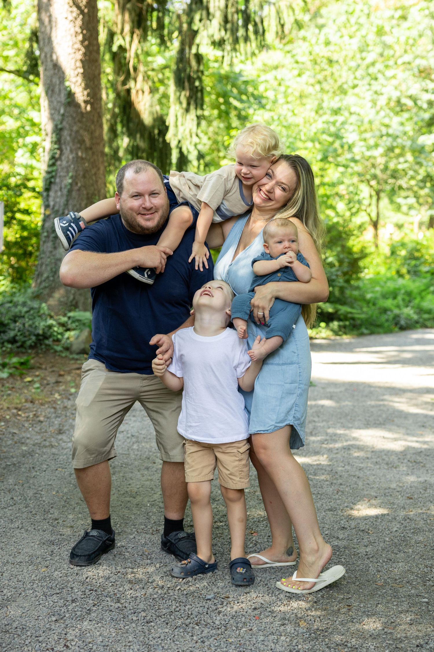 Happy family of five sharing joyful moments together on a tree-lined path.