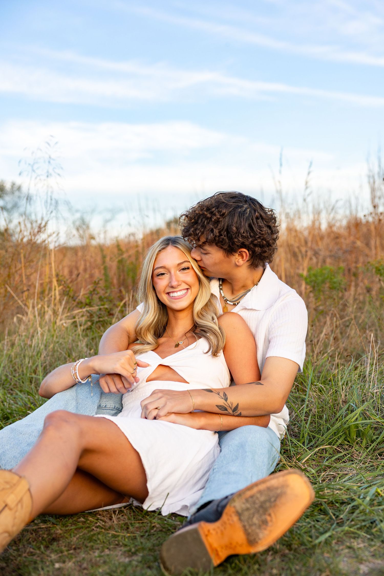 A couple lounges together in a sunny field sharing romantic moments.