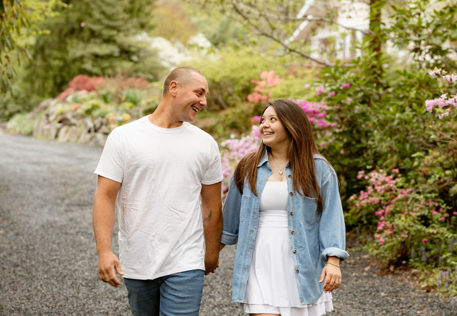 Couple walking hand in hand on a garden path surrounded by colorful blooming flowers and lush green trees.