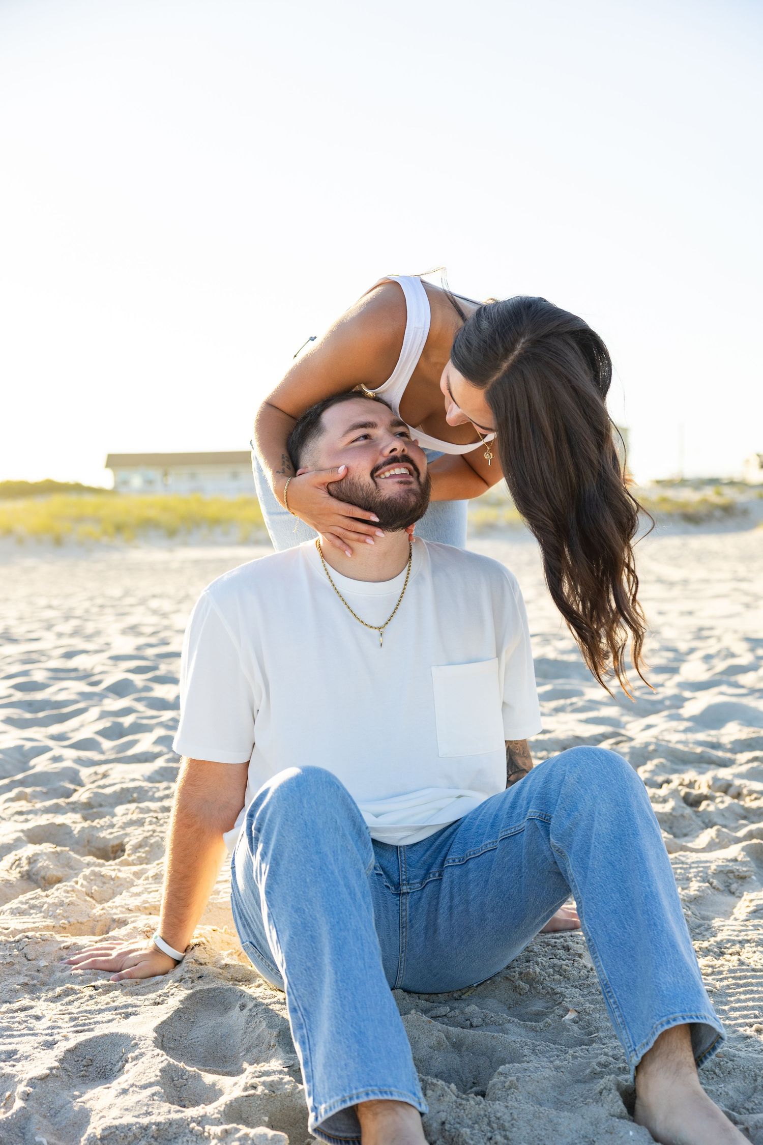 Playful couple photos on sandy beach wearing casual denim and white t-shirts.