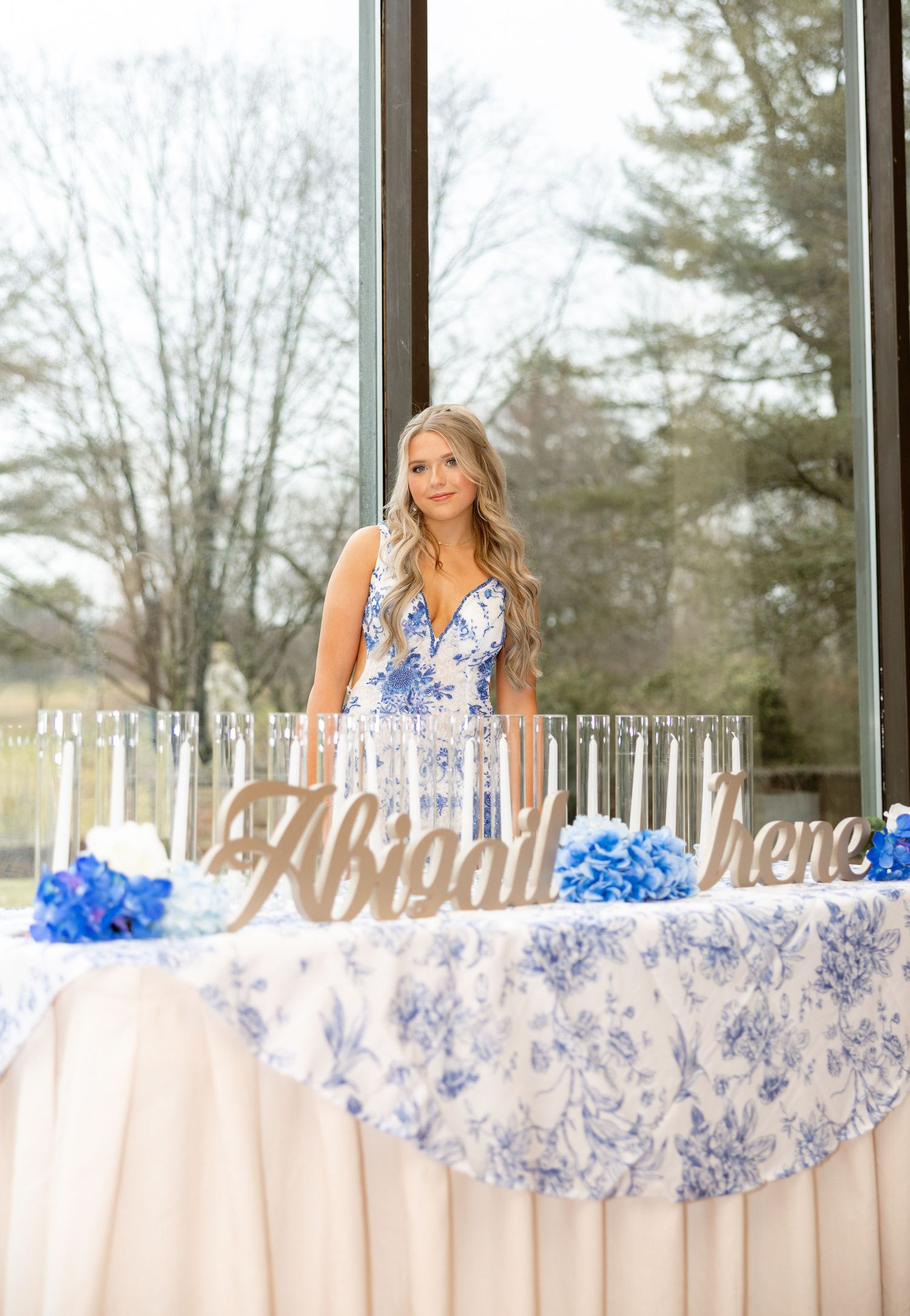 Young woman named Abigail Irene stands behind a floral blue and white decorated table at an elegant celebration event.