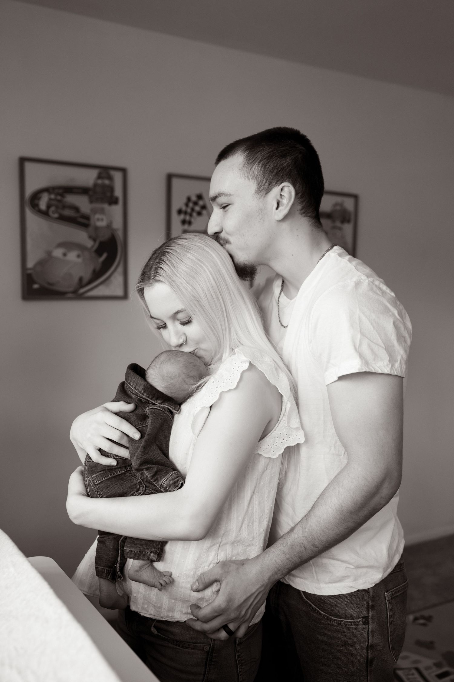 A tender black and white portrait of a couple embracing with their newborn baby in a cozy home setting.
