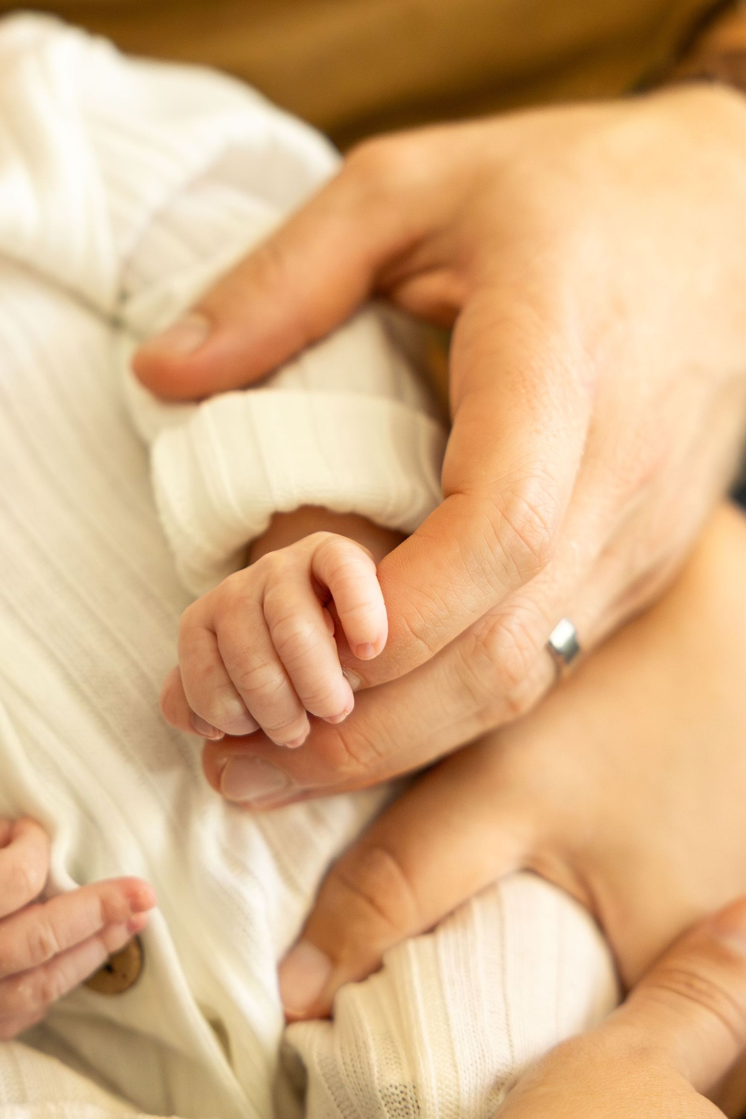 Newborn baby hand grasping adult finger, close-up of tiny infant fingers wrapped around parent's hand.