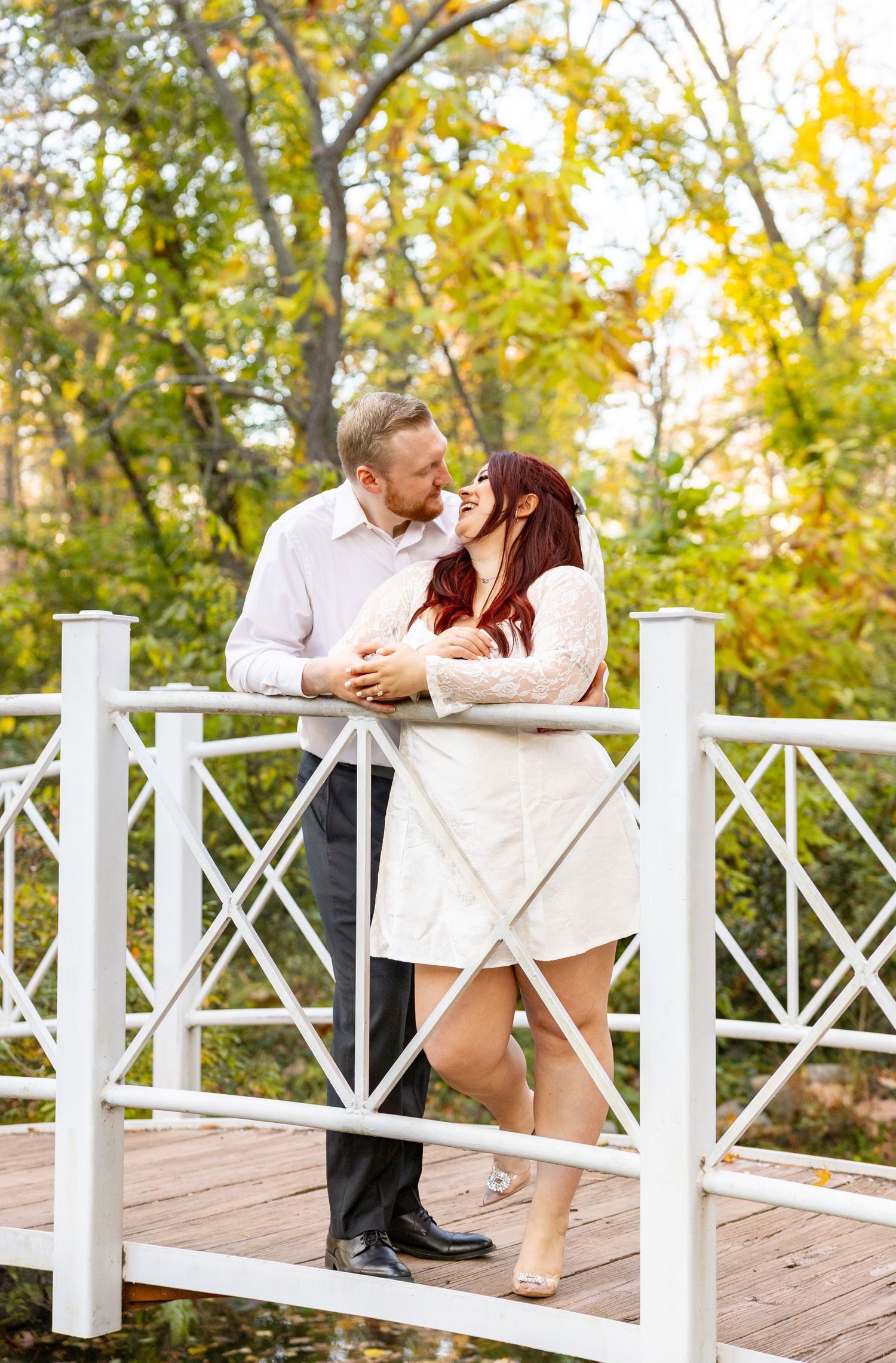 Romantic couple poses on white wooden bridge during autumn photo session.