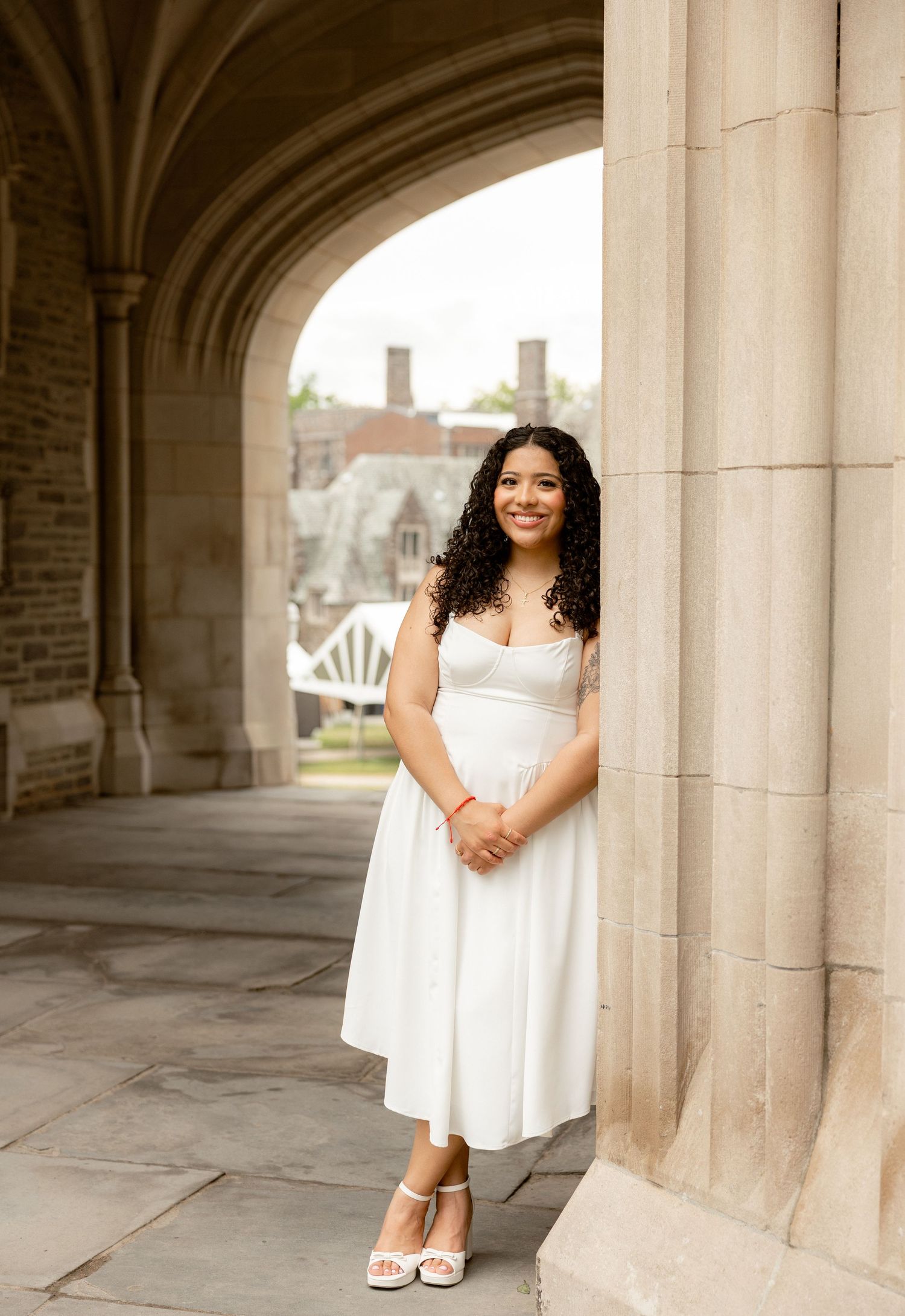 Young woman in white midi dress posing under stone archway at Princeton University campus.