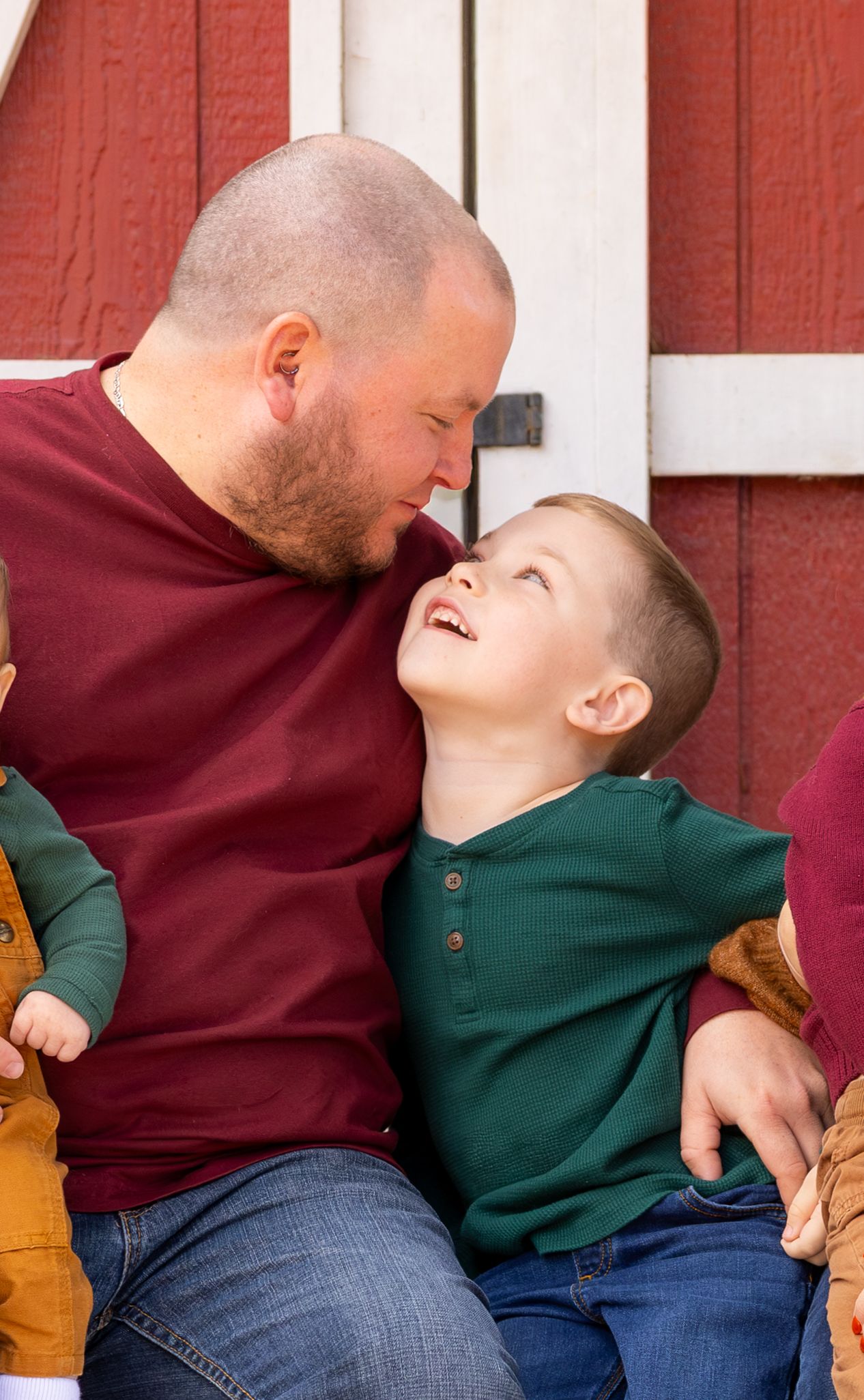 Playful family moment against red barn wall with joyful expressions.