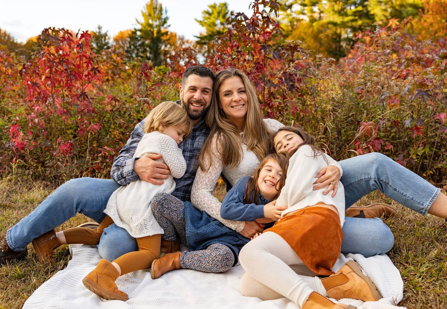 Family lounging together on a blanket surrounded by vibrant fall foliage.