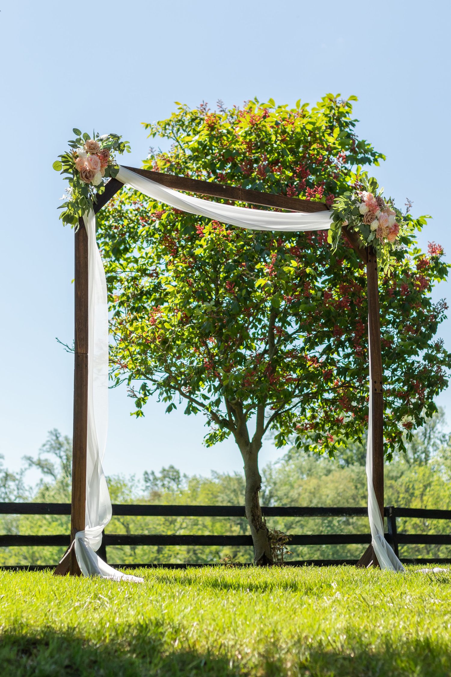 An outdoor wedding arbor decorated with white fabric and flowers against a blue sky.