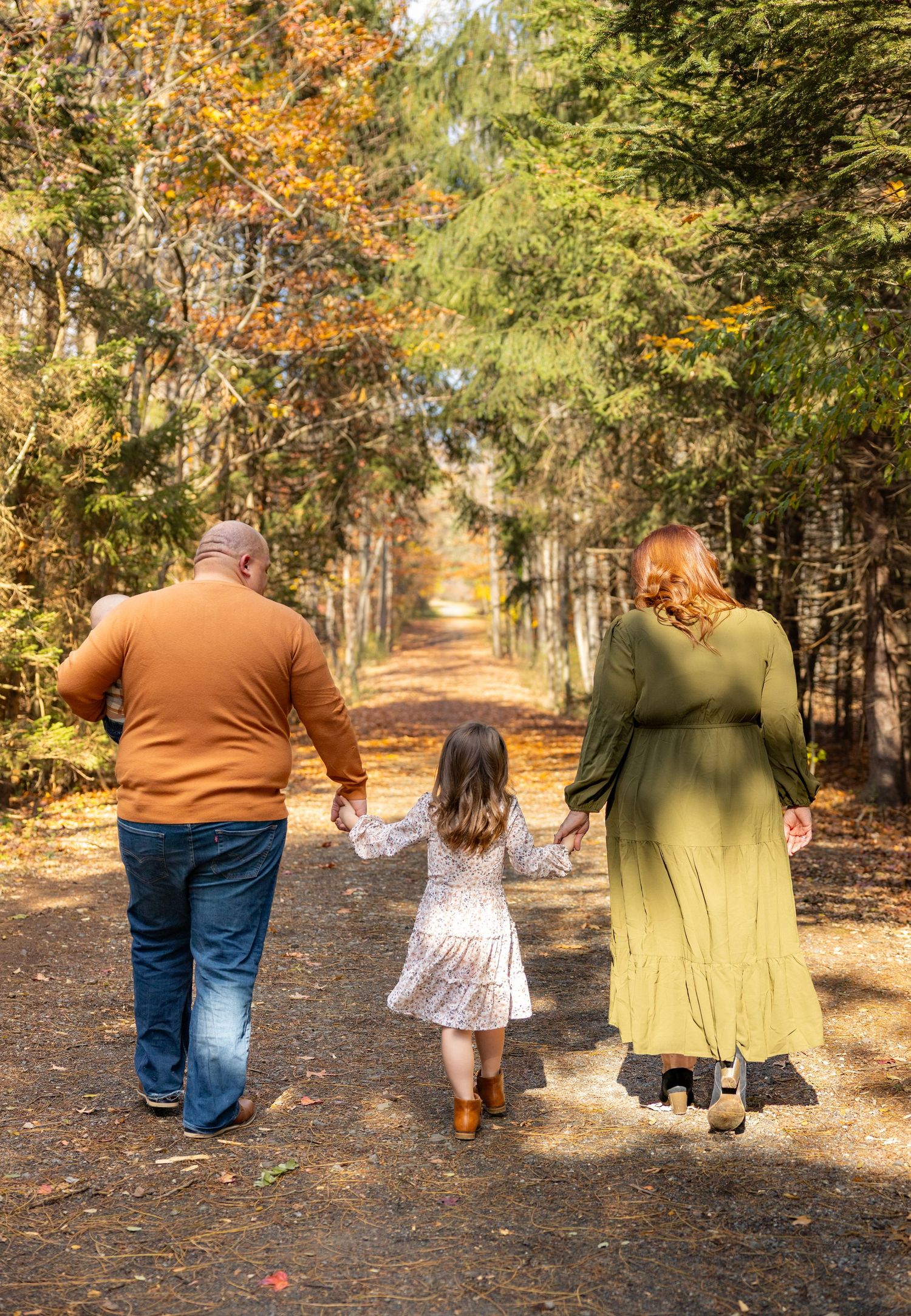Family walking hand in hand down a tree-lined autumn path.