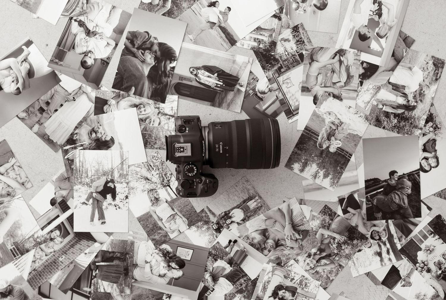 A DSLR camera surrounded by scattered black and white printed photographs on a white surface.