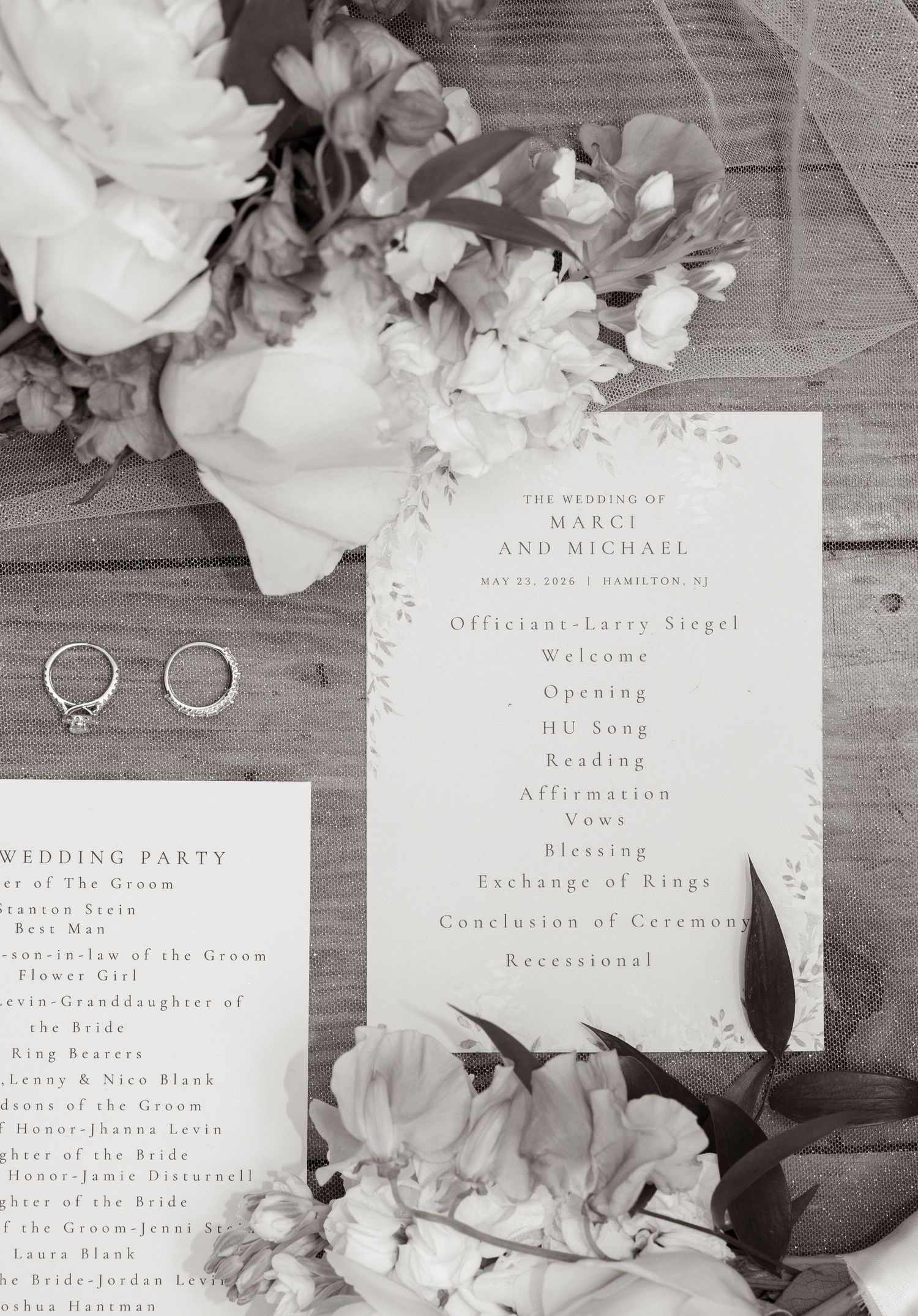 Black and white wedding program for Marci and Michael displayed with floral arrangements and wedding rings on a wooden surface.