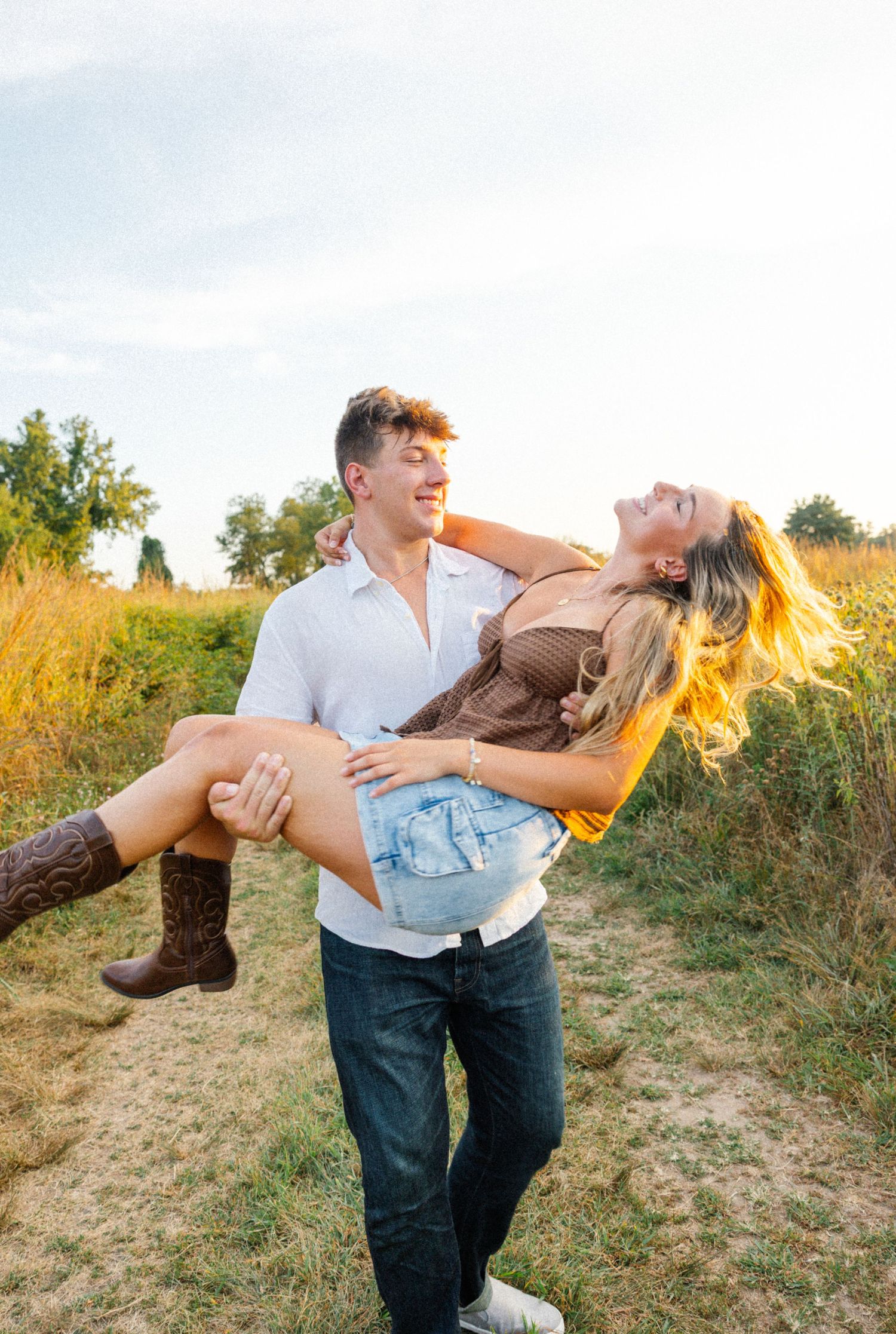 Playful couple in casual attire sharing a romantic moment in a sunlit field.