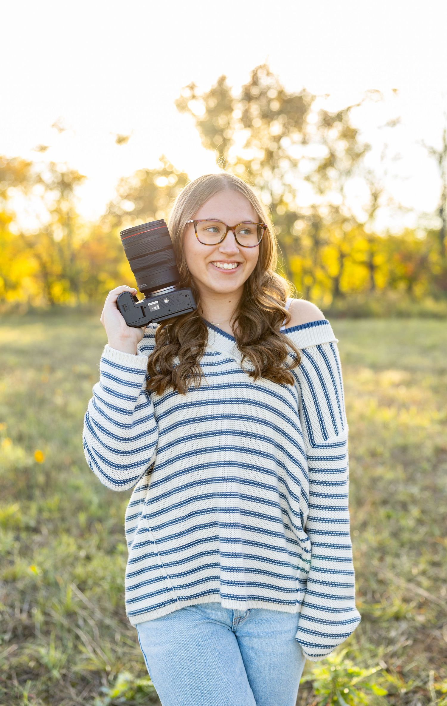 Casual outdoor portrait wearing a blue and white striped sweater with glasses against a golden sunset background.