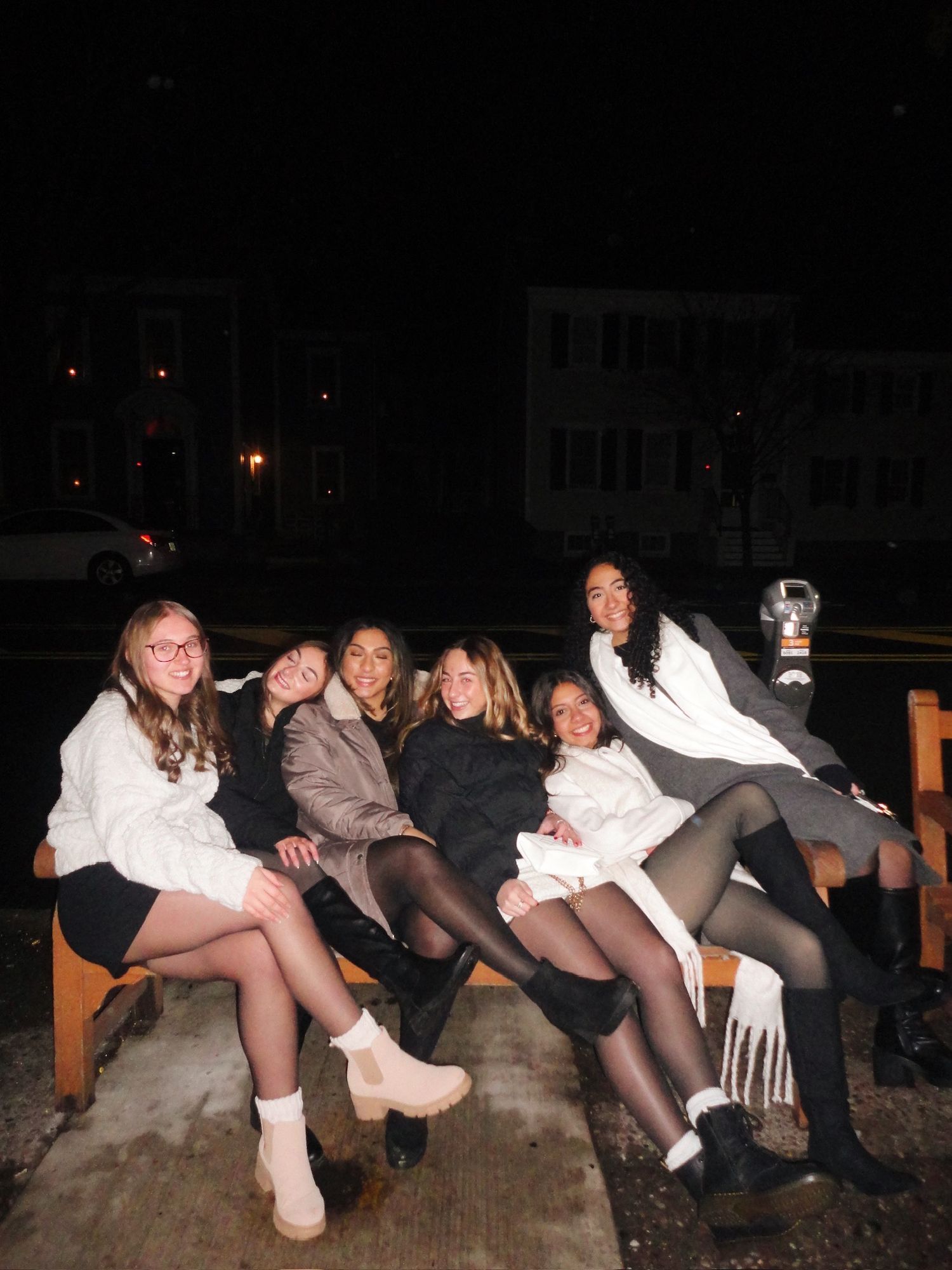 A group of people sitting together on the ground at night in casual attire.