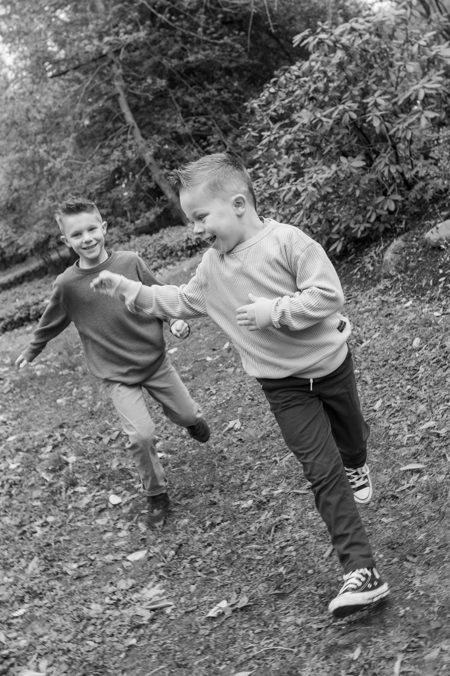 Two boys laughing and running together on a forest path in a black and white outdoor photo.