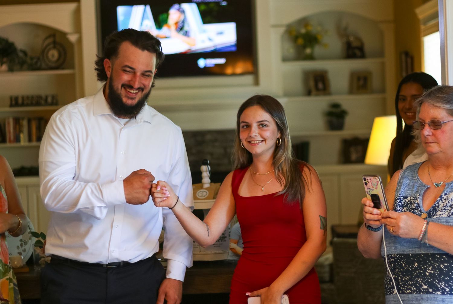 Wedding guests socialize in a casual indoor setting with TV in background.