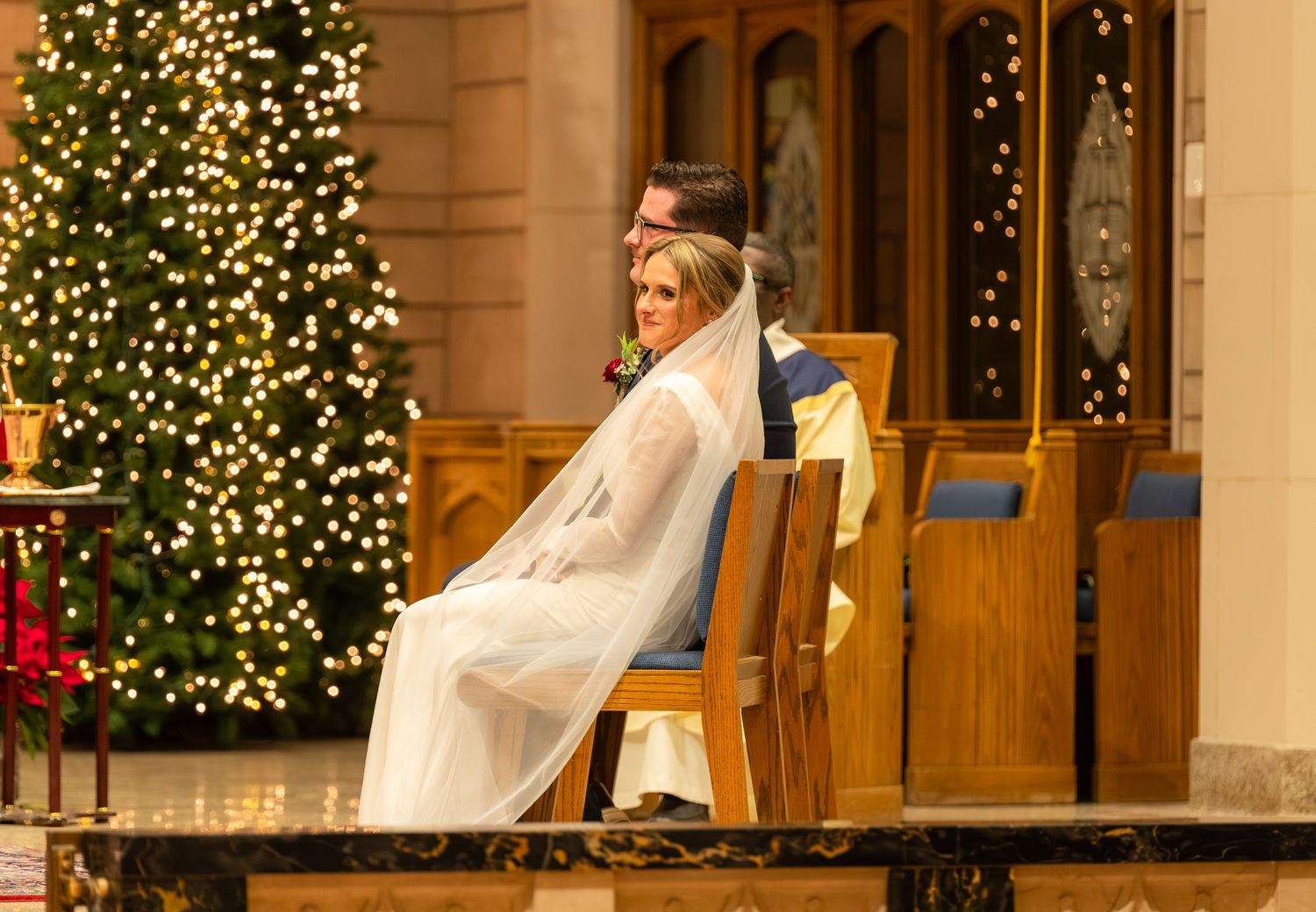 Wedding ceremony in a church decorated with illuminated Christmas trees and festive lights.