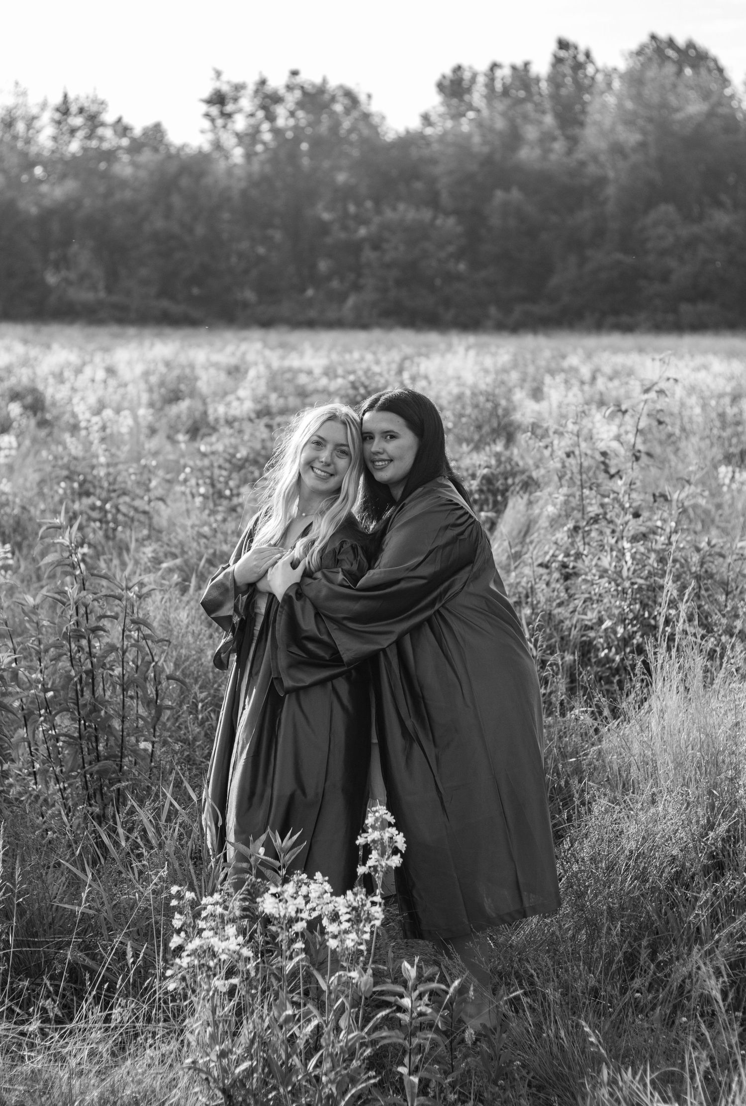 Two figures in dark cloaks embrace in a dreamy black and white field of flowers.