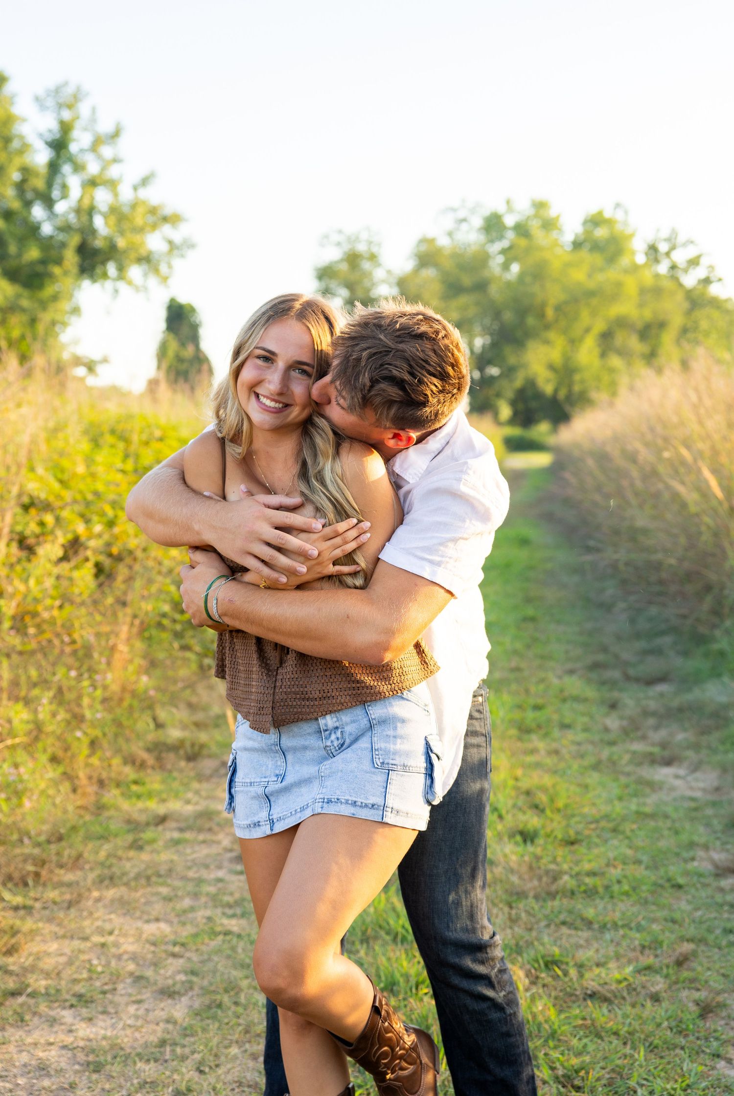 Playful couple photography session on a sunny dirt path surrounded by greenery.
