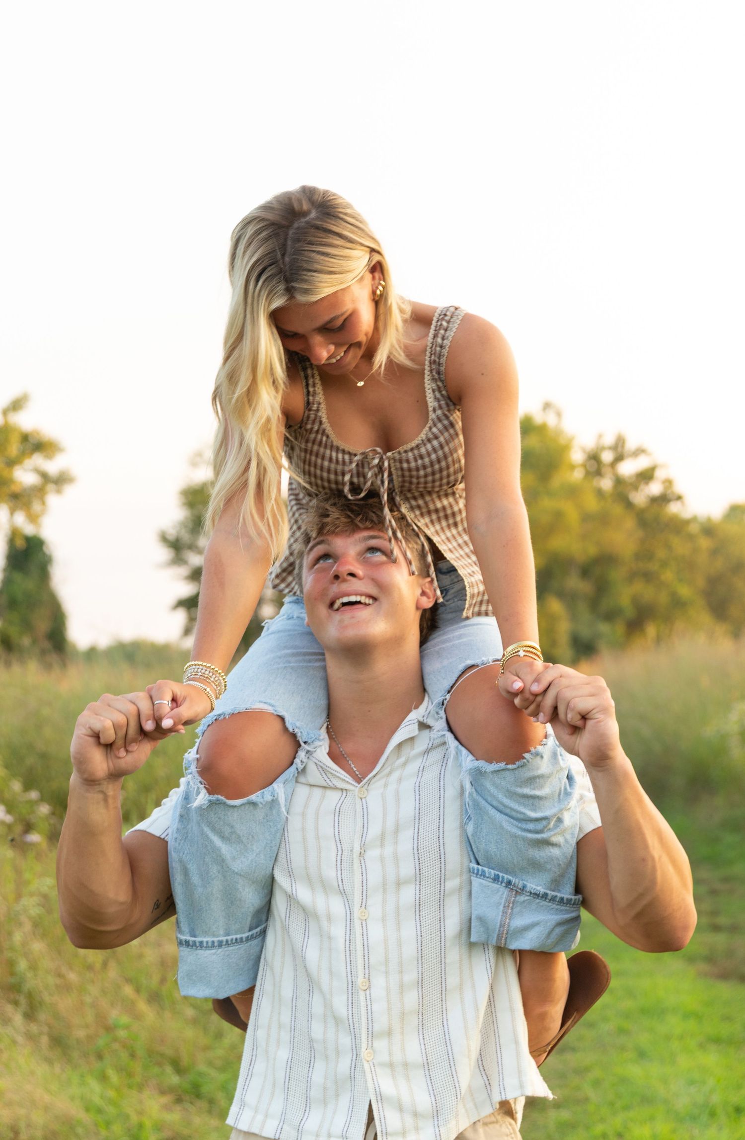 A playful couple enjoys a piggyback ride in a sunny field during summer.