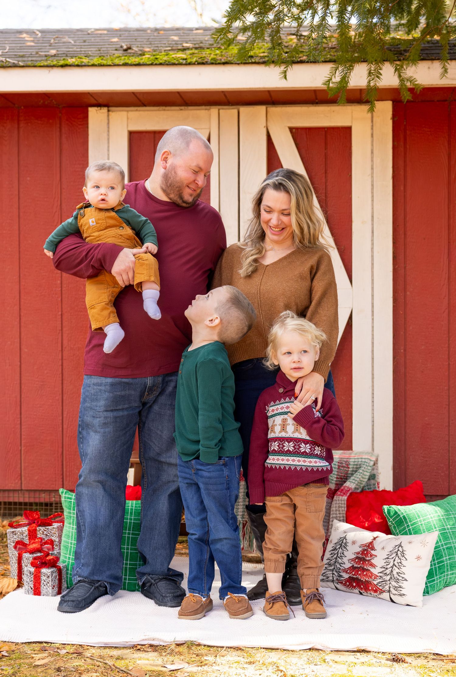 Family portrait session with holiday decor against rustic red barn backdrop.