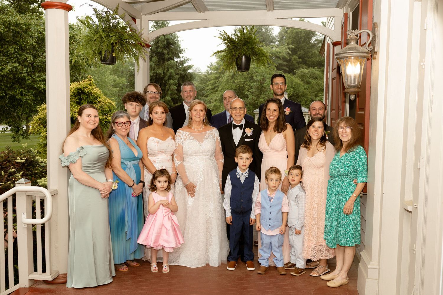 Large wedding family portrait on a decorated porch, featuring bride, groom, and guests in formal attire.