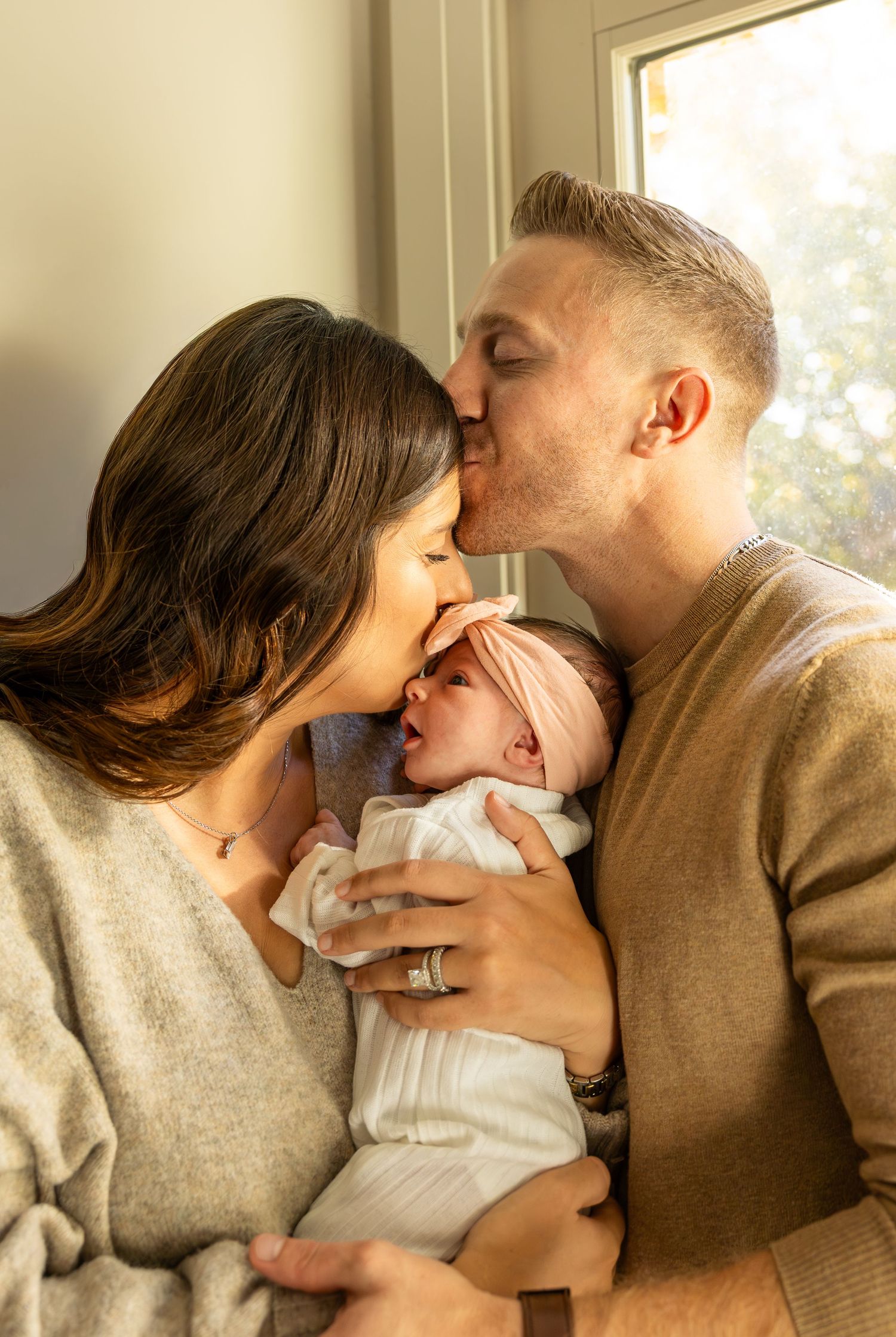 Tender family moment with newborn baby being held and kissed in warm lighting.