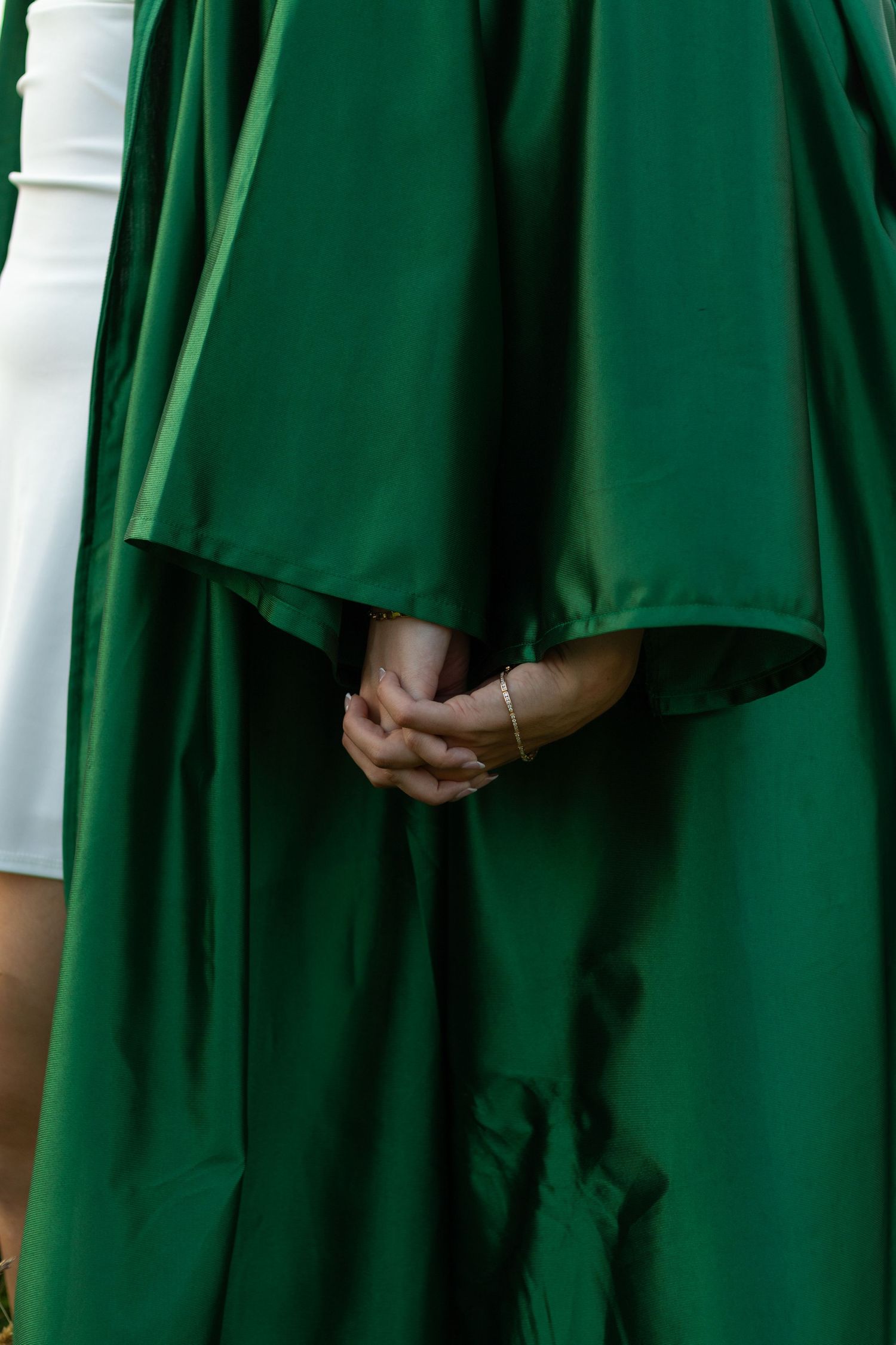 Close-up detail of hands clasped beneath flowing green graduation gown.