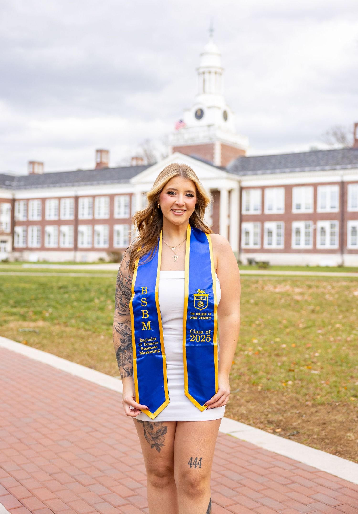 Graduate wearing blue and gold honors stole poses on campus brick walkway.