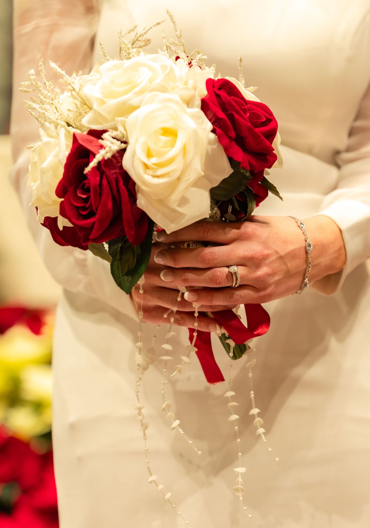 Bridal bouquet featuring red and white roses held against white wedding dress.