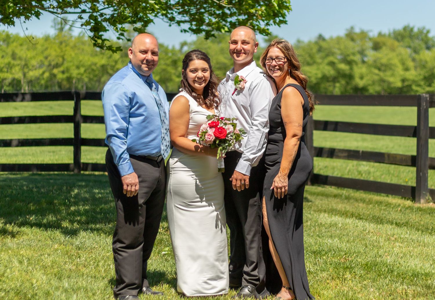 Wedding party poses on a grassy hill with black fence in background.