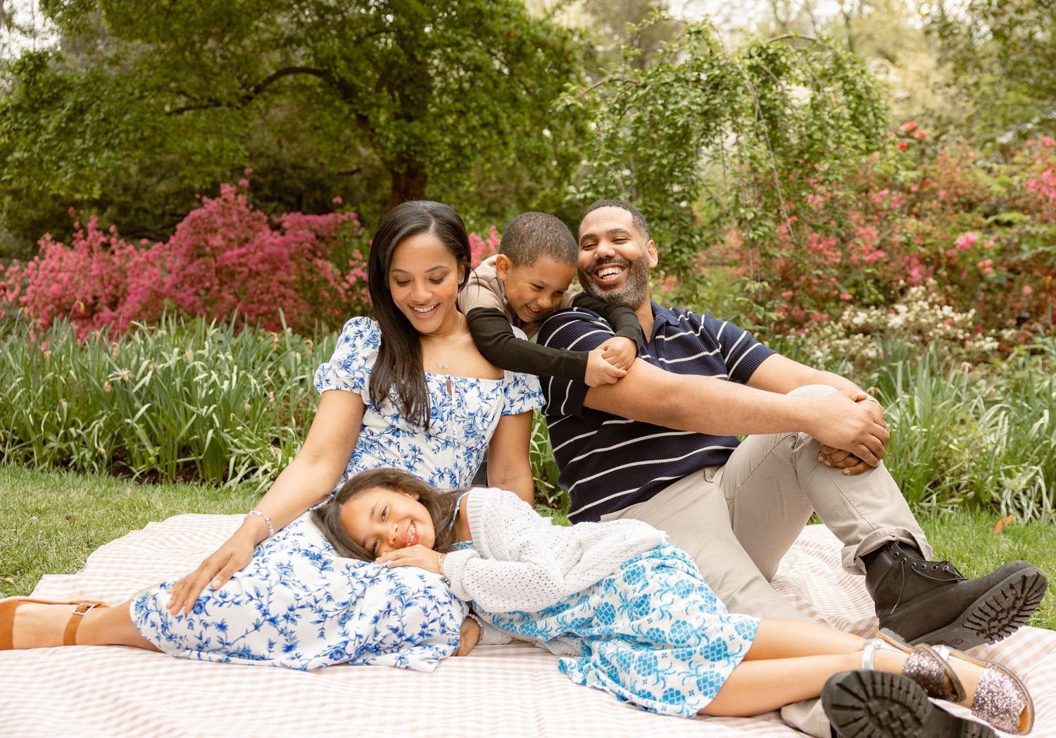Happy family of four enjoying a sunny outdoor picnic on a blanket surrounded by lush green and red foliage.