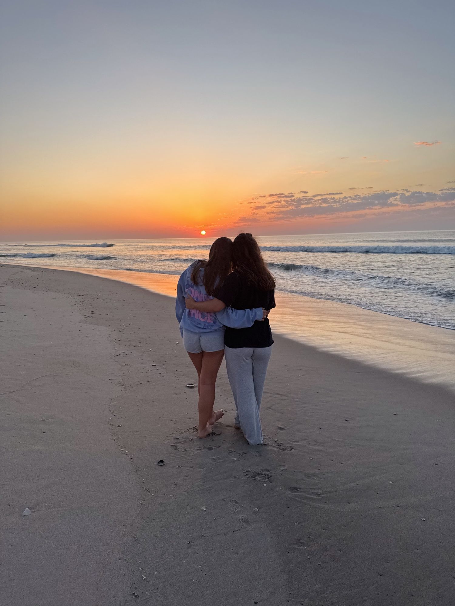 Couple silhouetted against vibrant beach sunset watching waves roll in.