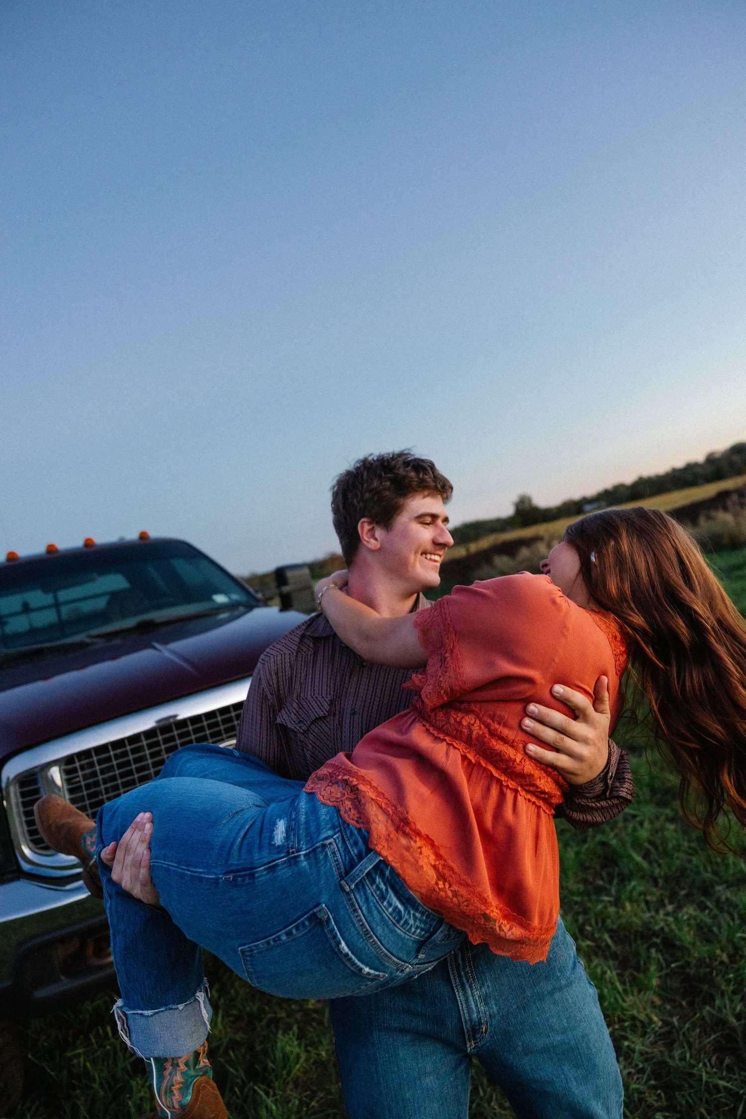 Romantic sunset photoshoot with couple in casual wear near parked cars.