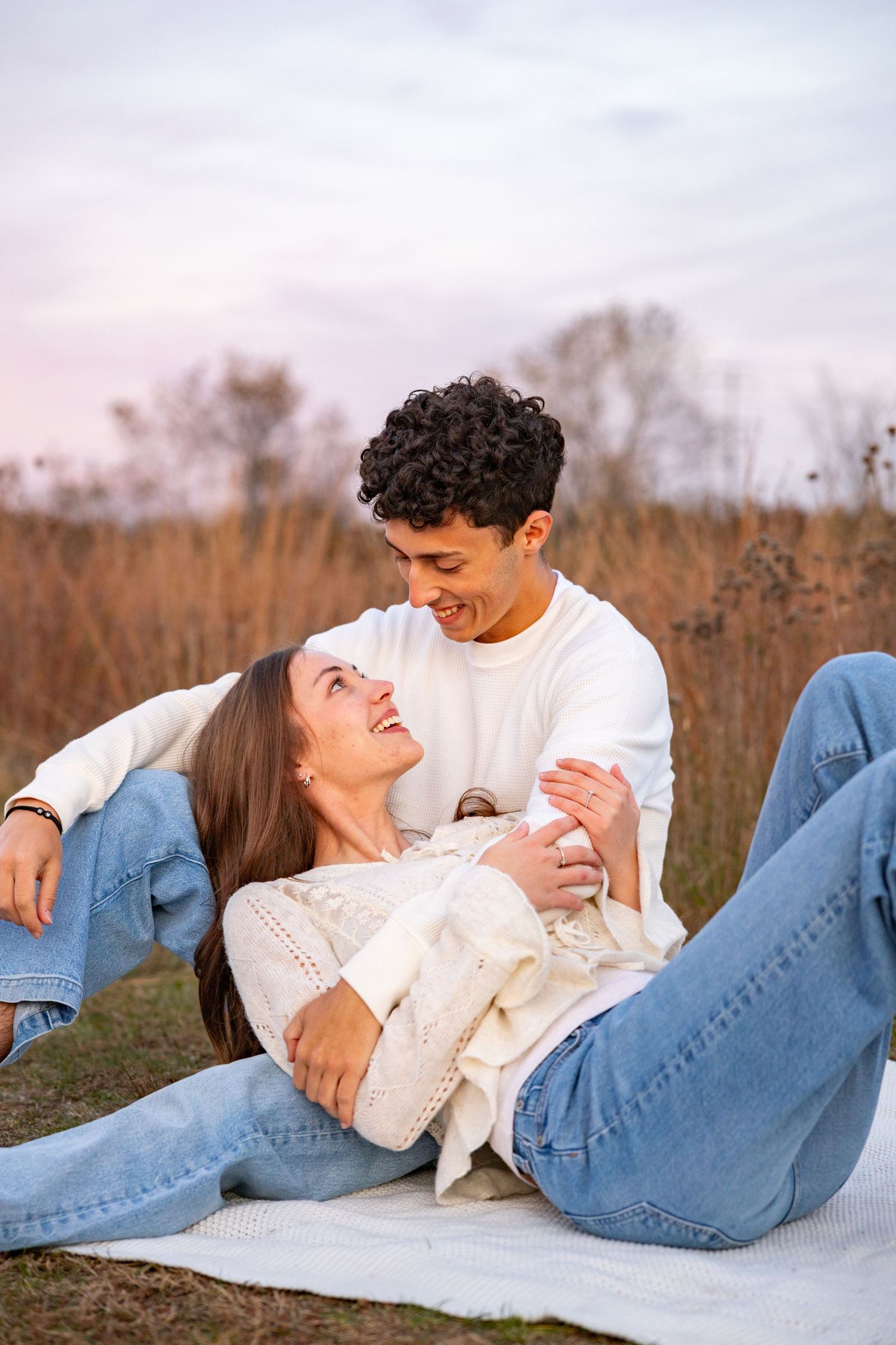 Romantic couple in casual outfits lying together in autumn field during sunset.