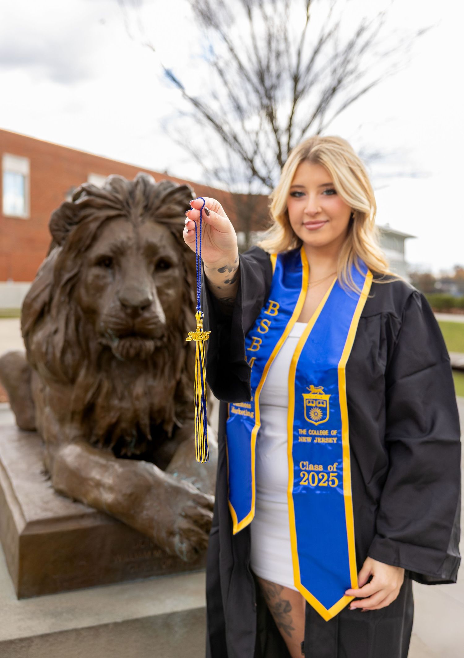 Graduate in FFA stole poses with lion statue on campus.
