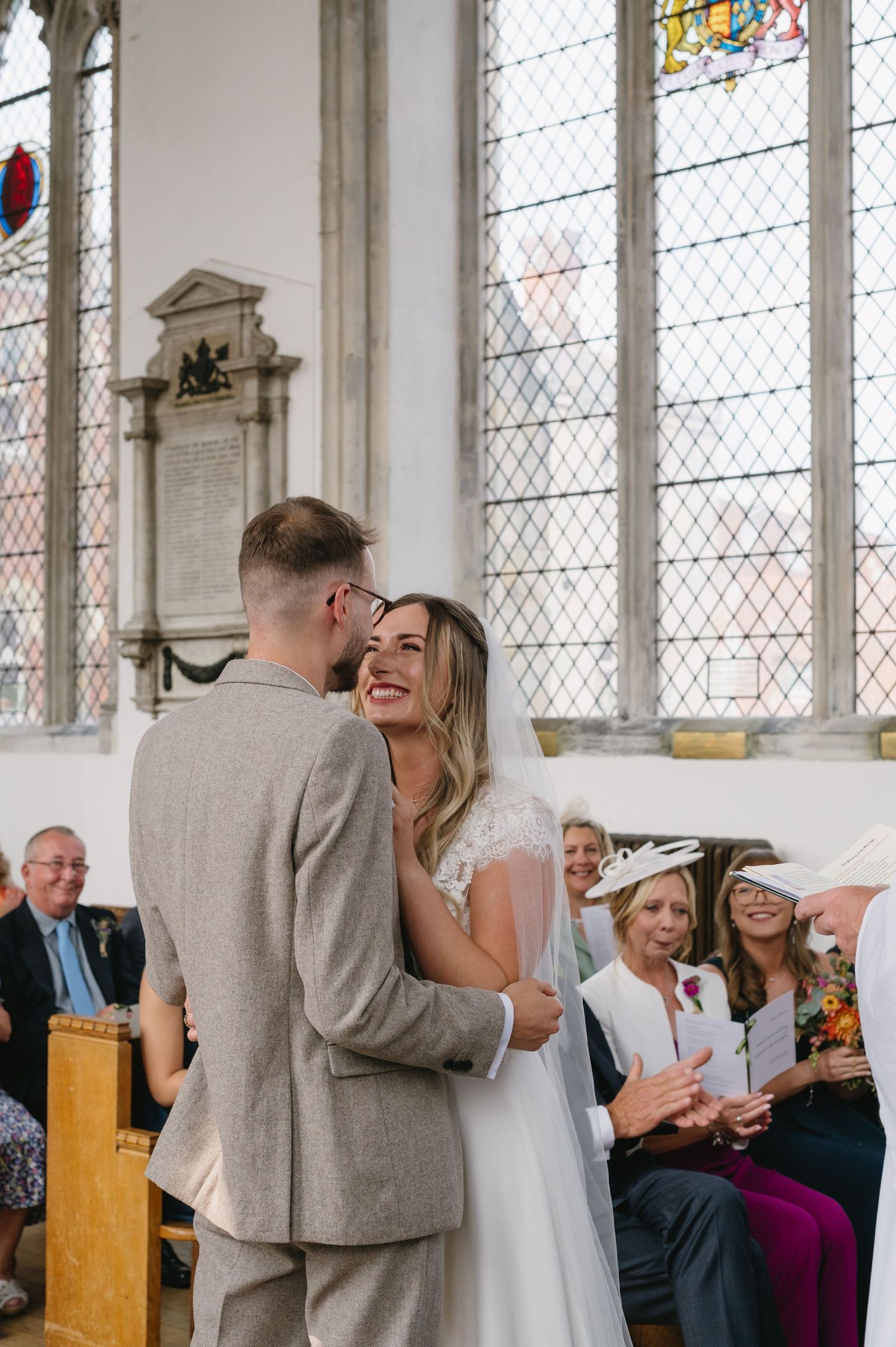 Bride smiling at groom during church wedding ceremony with stained glass windows behind.