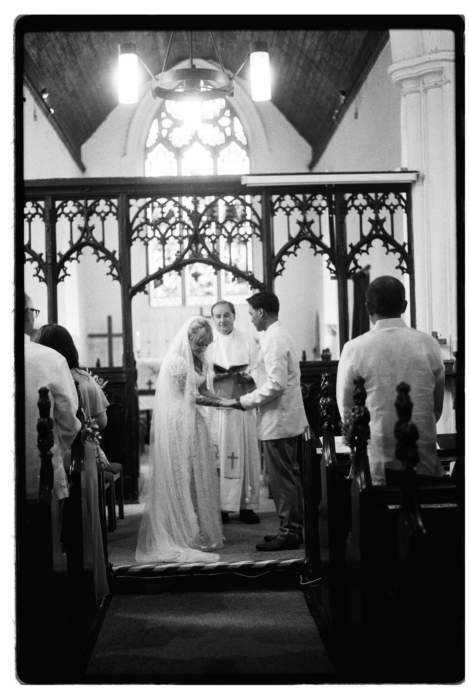 Black and white film photo of wedding ceremony at church altar with officiant.