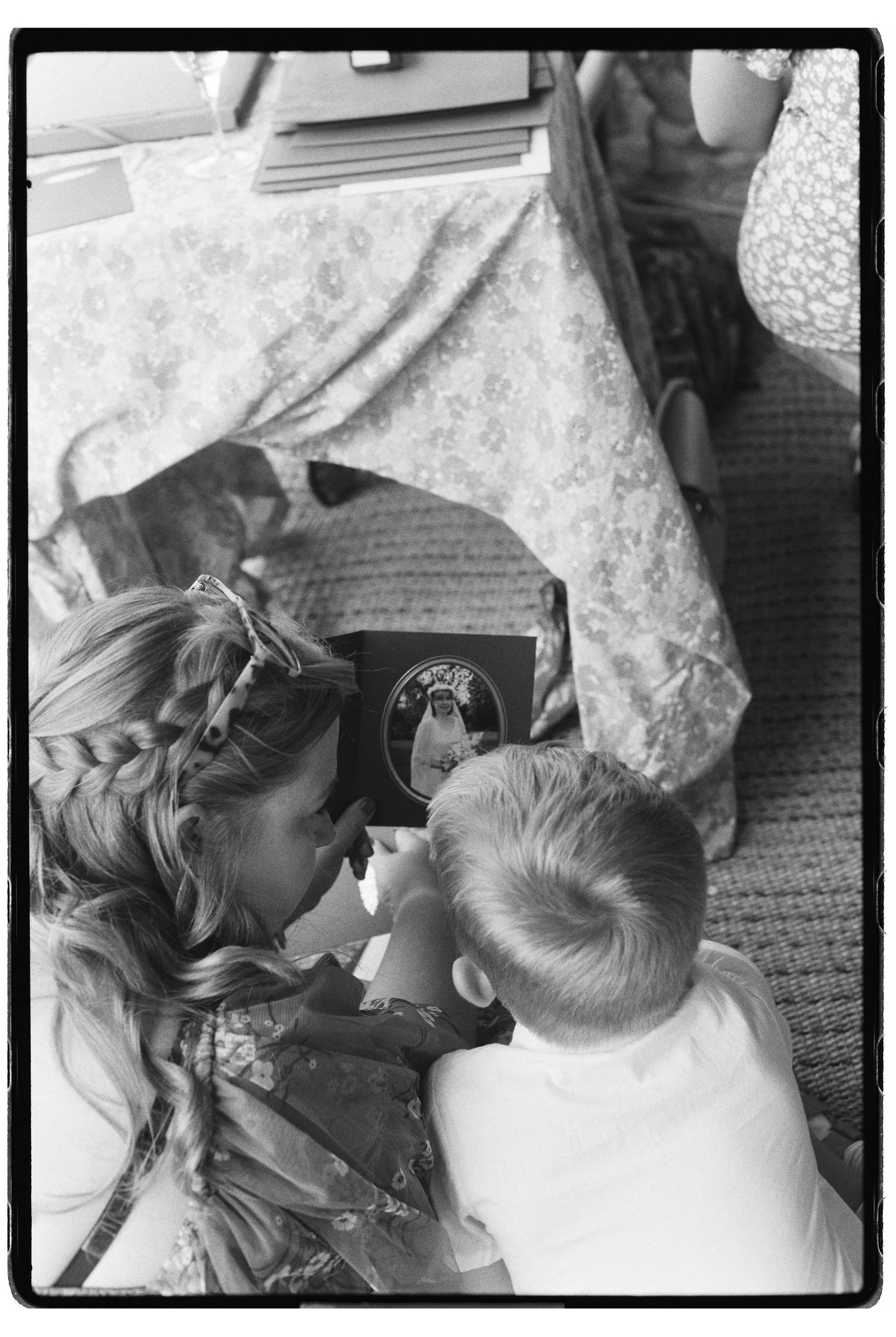 Overhead black and white film photo of a woman and young child looking at a book together on the floor.