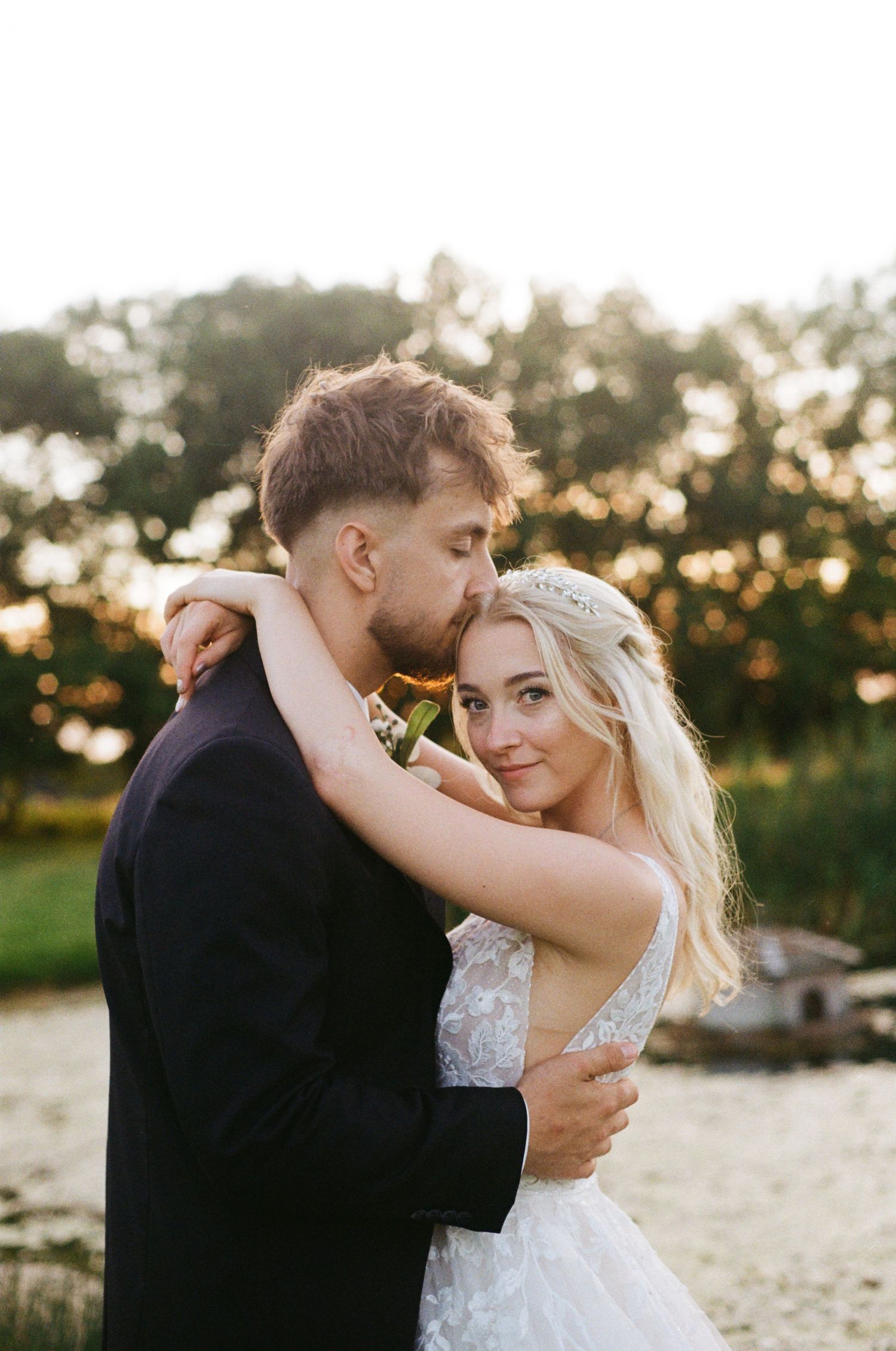 Bride and groom share a tender embrace outdoors at golden hour, with the bride smiling at the camera.