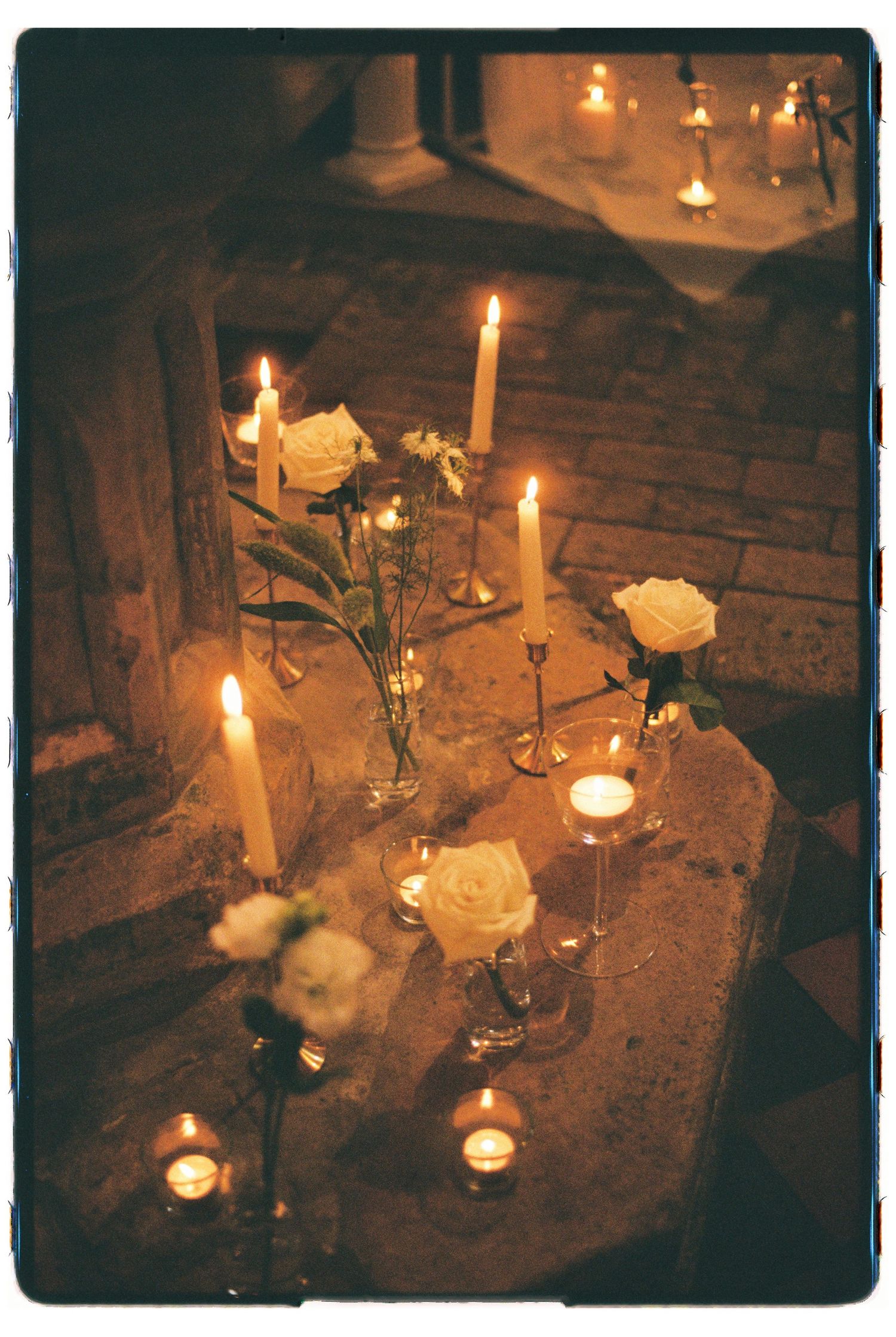 Romantic candlelit wedding altar with white roses, taper candles, and tea lights on stone steps.