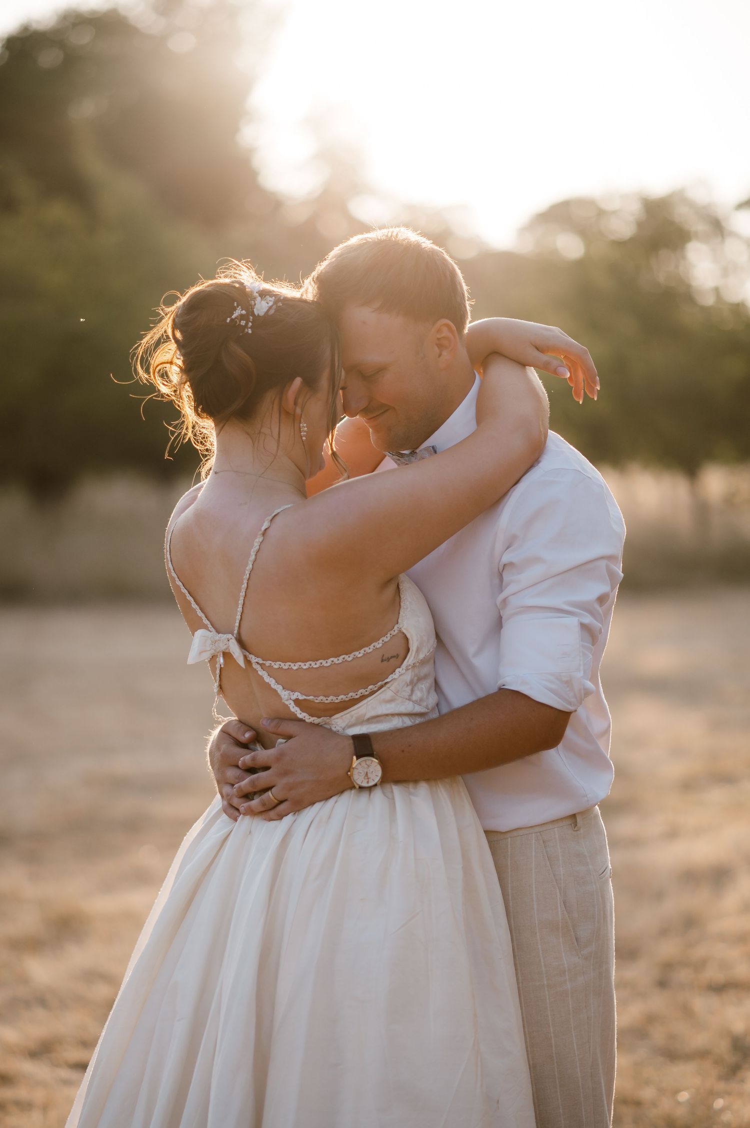 Newlyweds embracing intimately in a sunlit golden field during a romantic wedding photo session.