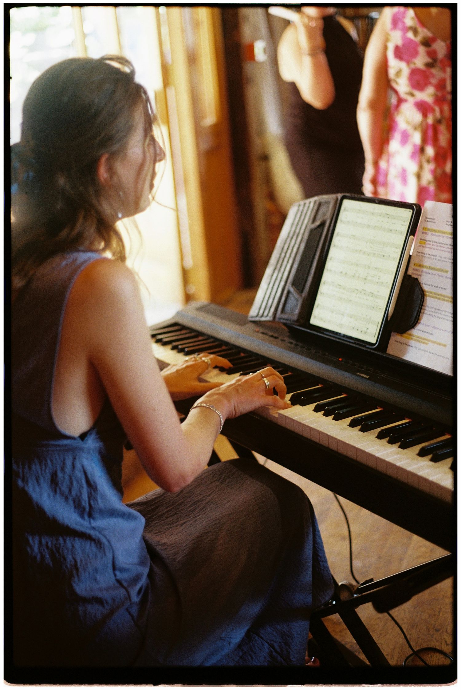 Woman in blue dress plays keyboard piano at a wedding ceremony with sheet music on display.