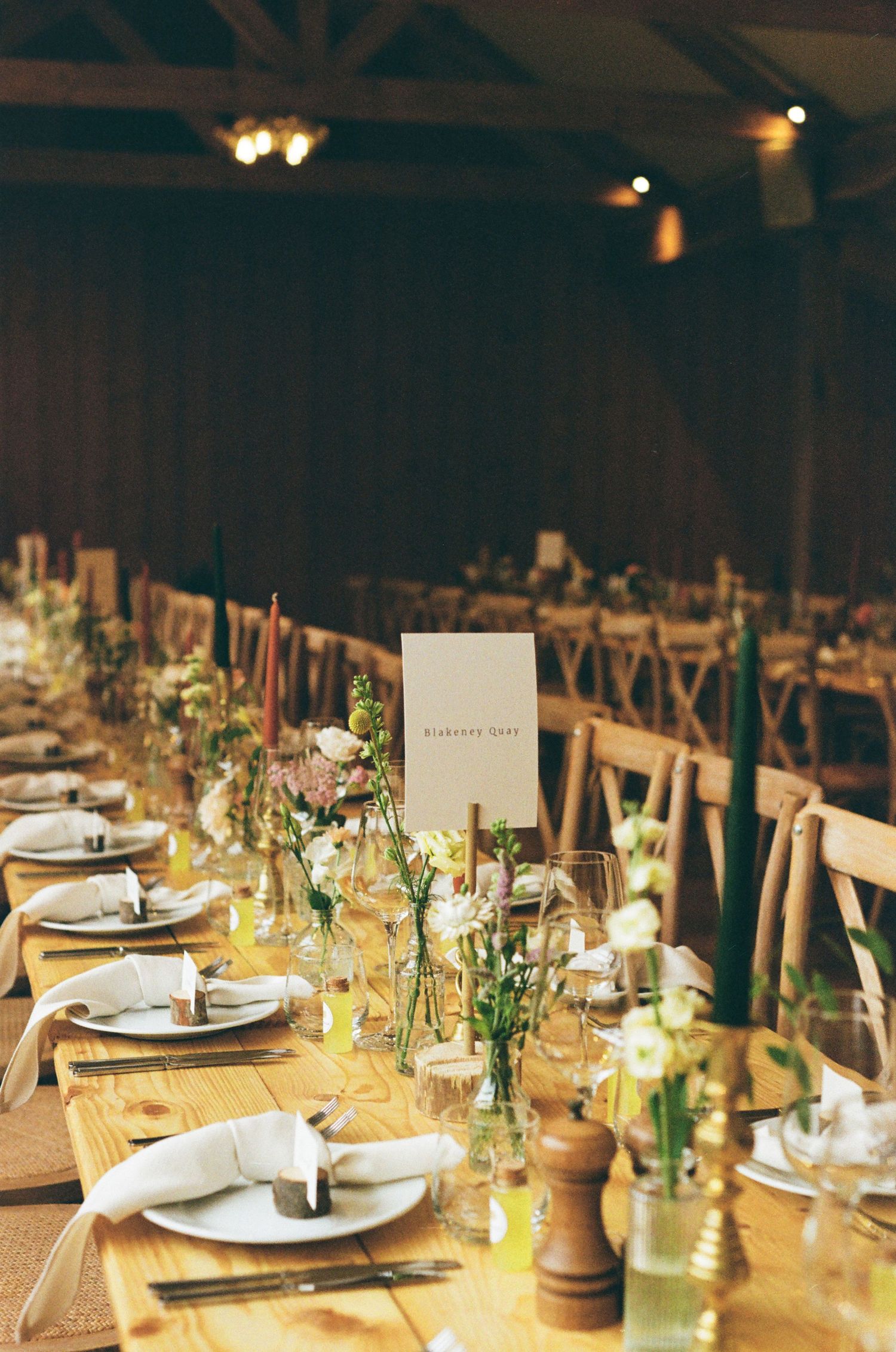 Rustic barn wedding reception with long wooden tables, green taper candles and wildflower centerpieces.
