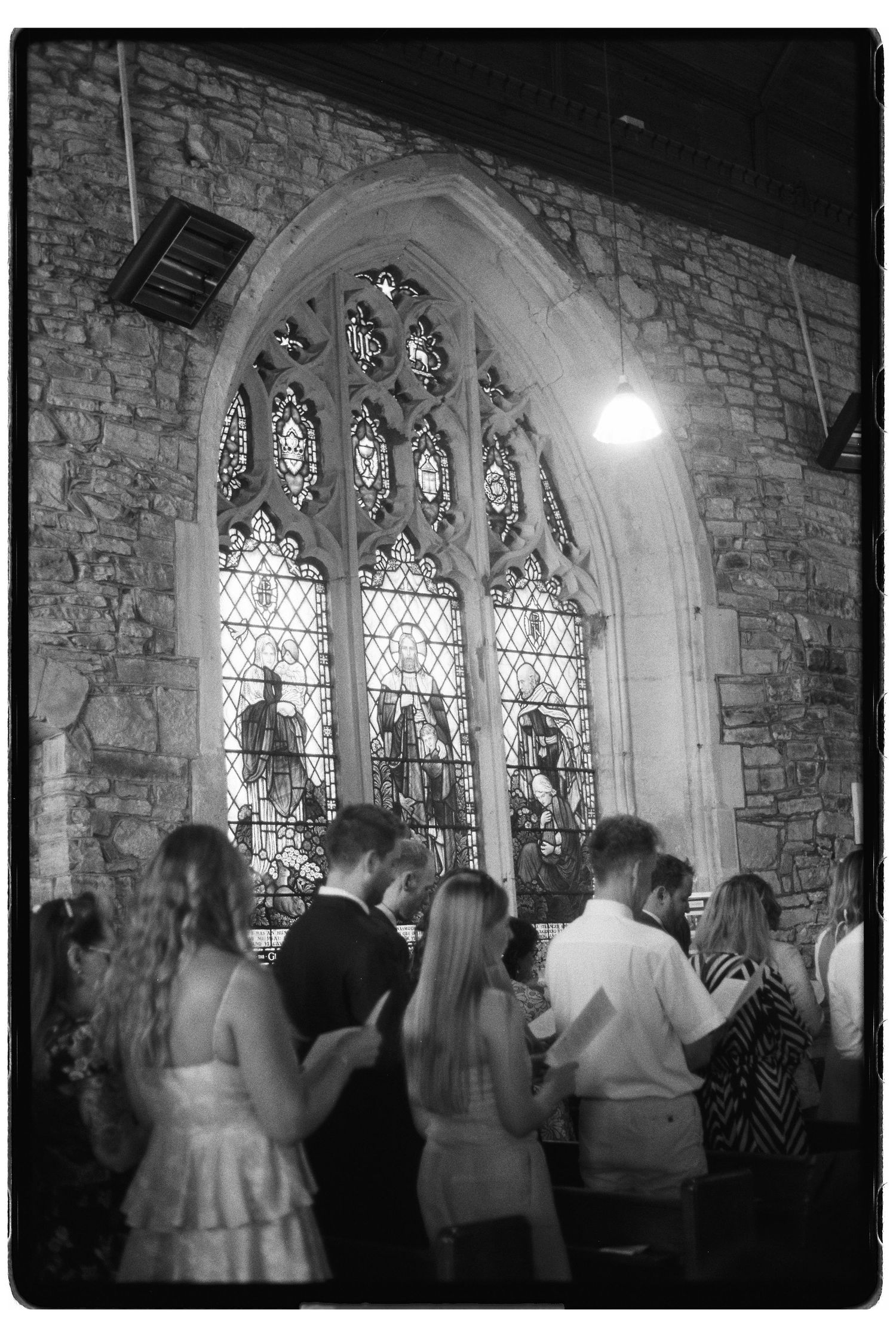 Black and white photo of wedding guests gathered inside a stone church with stained glass windows.