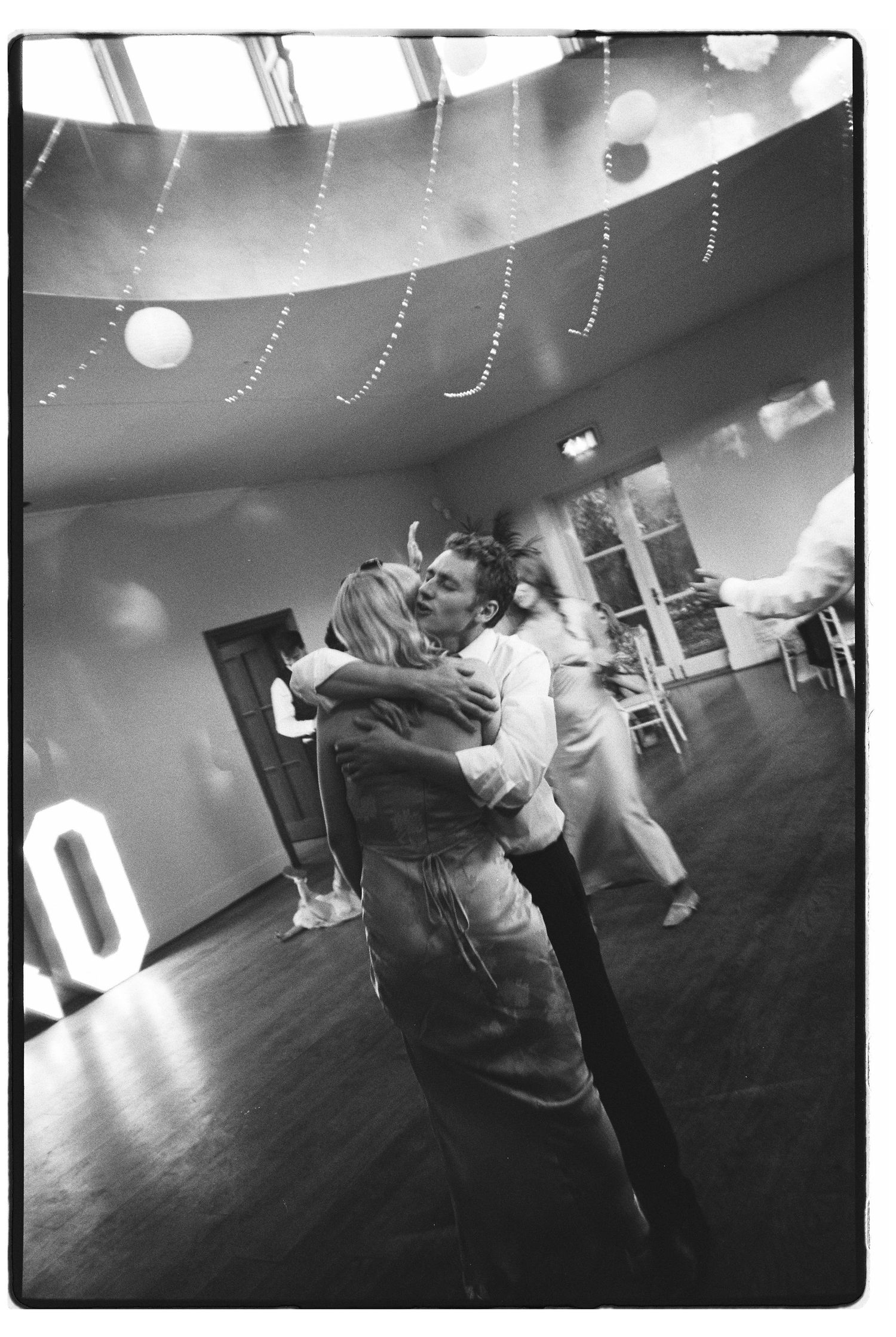 Couple sharing a romantic slow dance embrace at a wedding reception with decorative hanging lights.