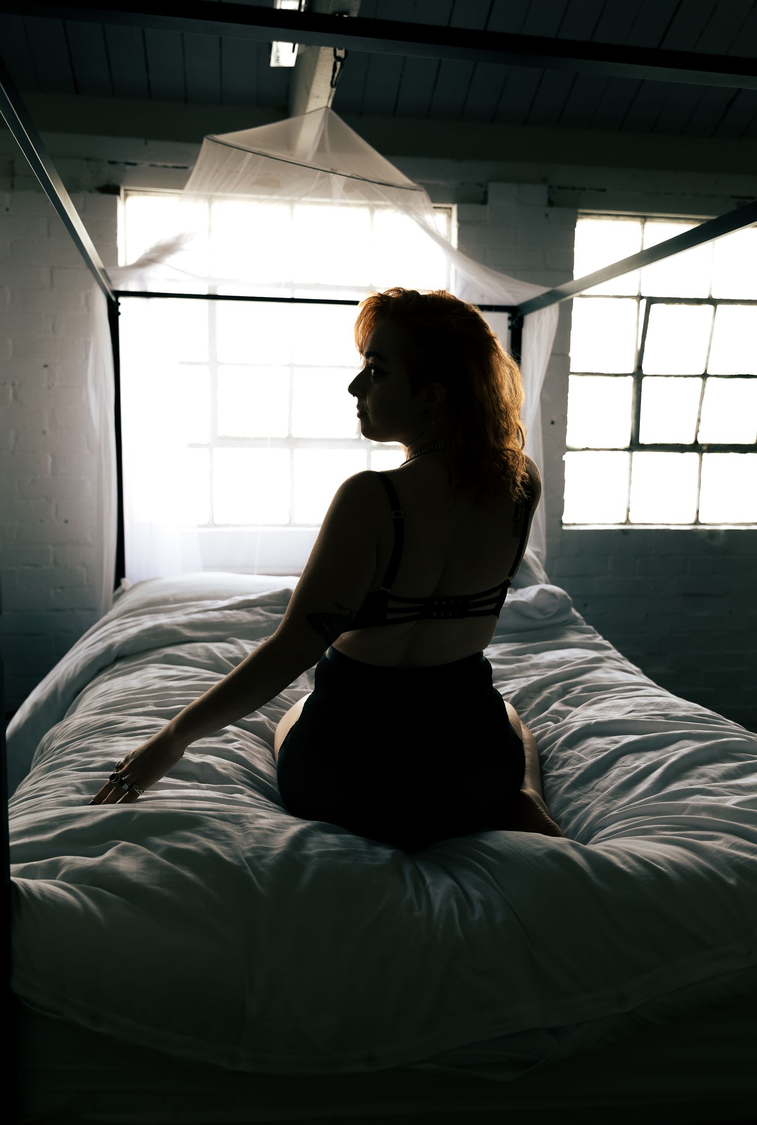 Silhouette portraits on white bedding with dramatic window lighting.