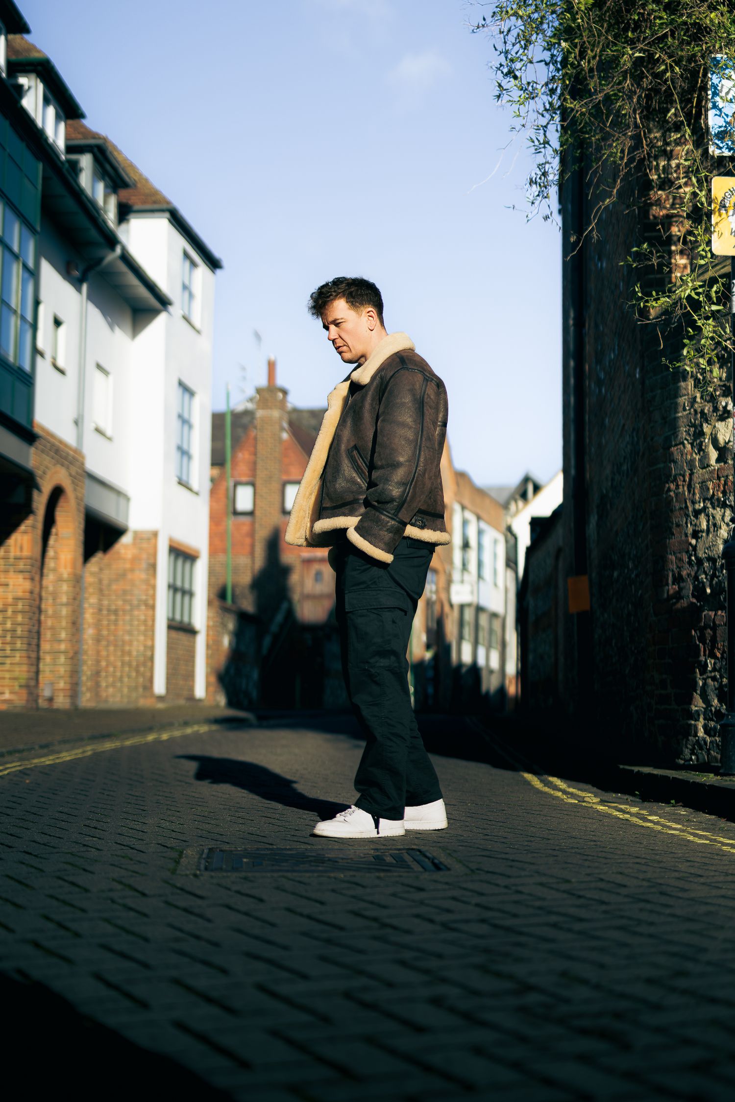 Side-profile street portrait of a man in a shearling jacket, morning light and city background