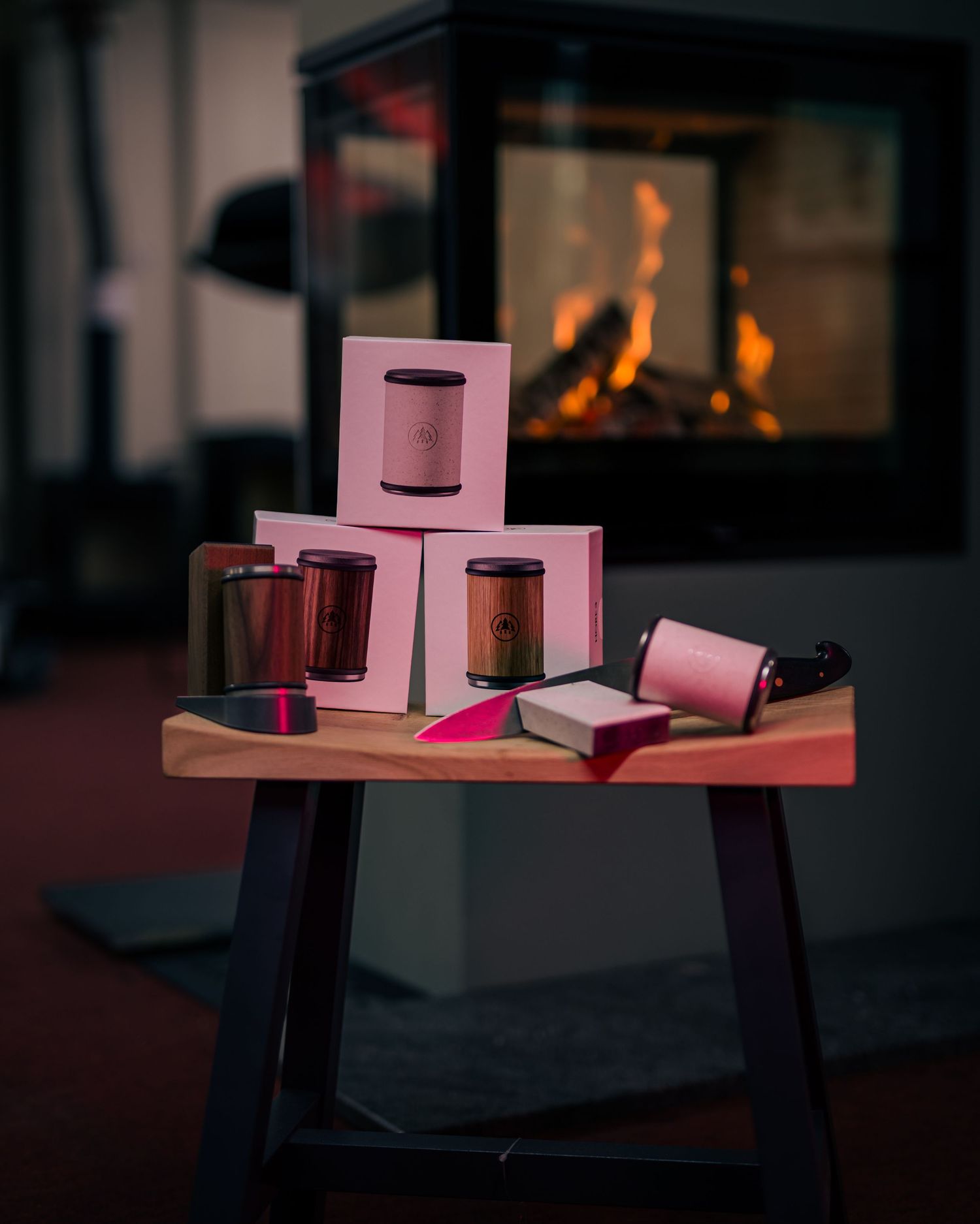 Knife-sharpening set and accessories arranged on a small wooden table, with boxed sharpeners and a chef’s knife; warm fireplace glow in the