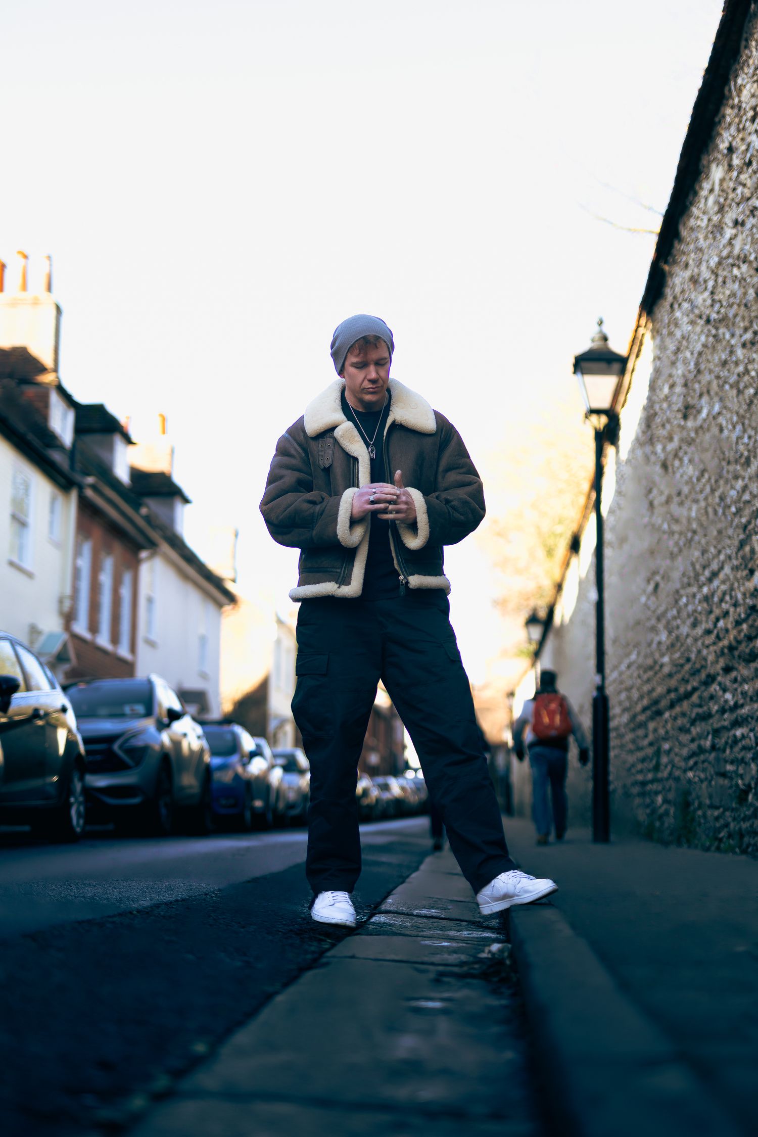 Full-body street portrait of a man in a shearling jacket standing in an urban lane
